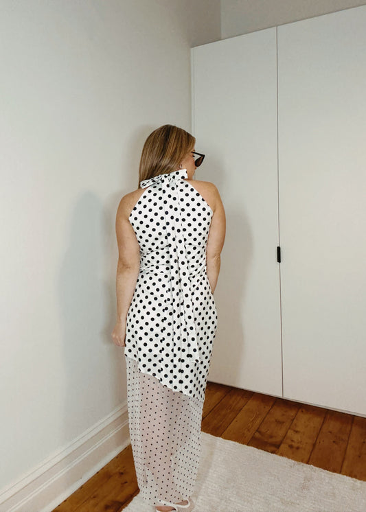 Woman in a polka dot dress standing in a room with white walls and wooden flooring.