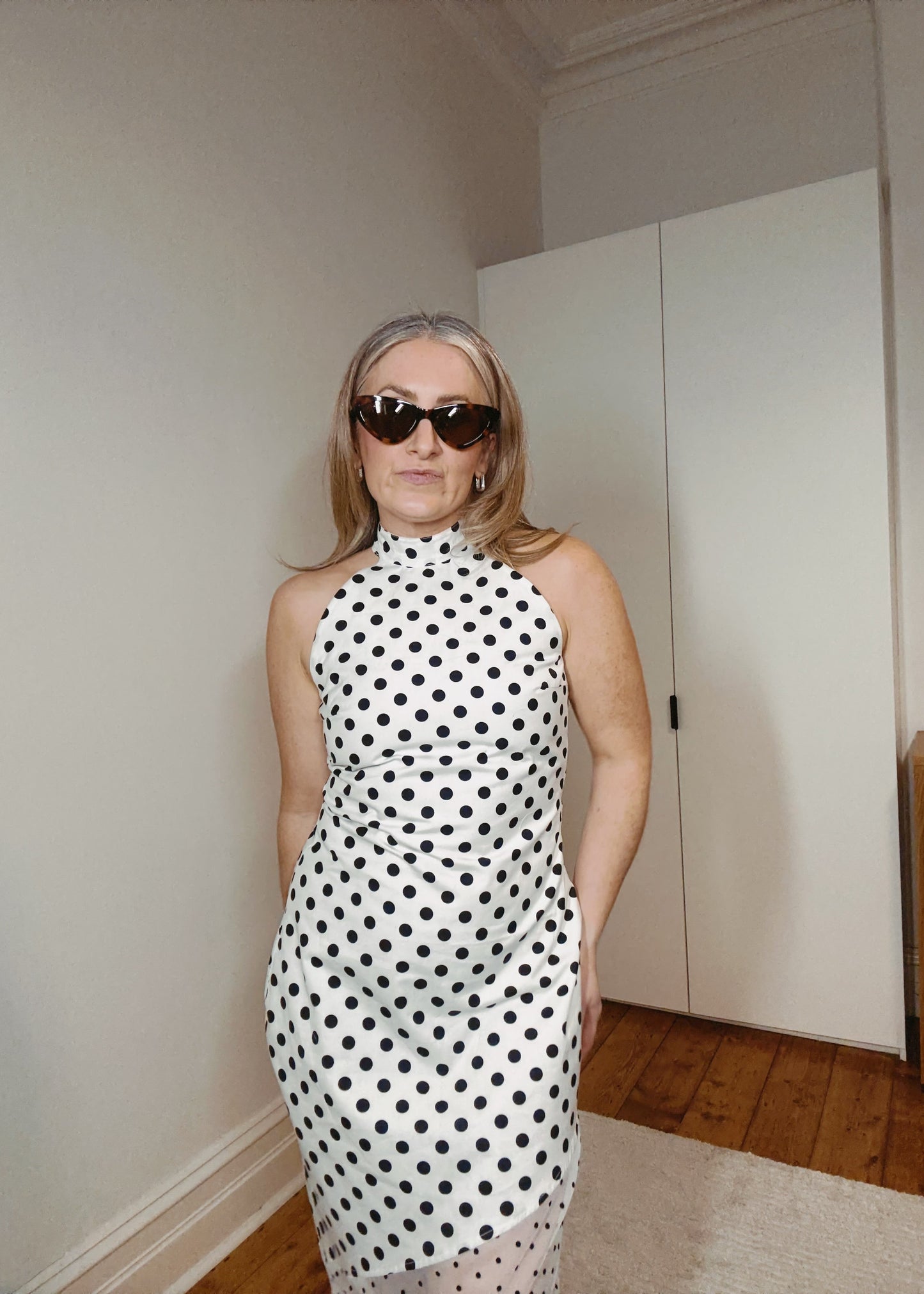 Person wearing a black and white polka dot dress in a room with a wardrobe.