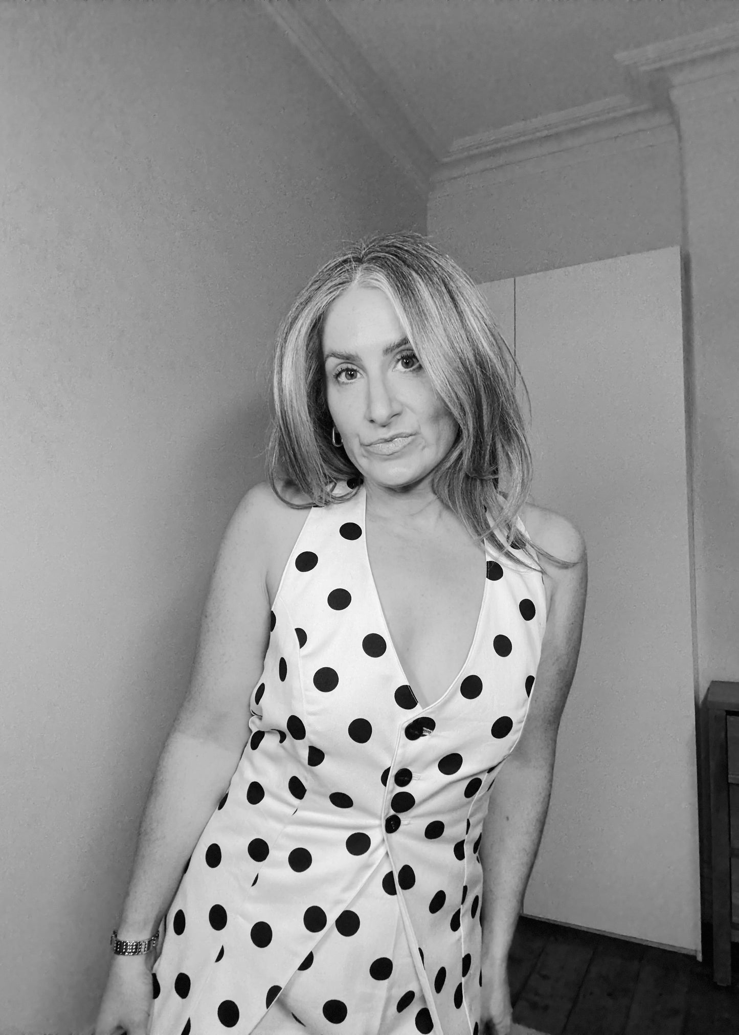Woman wearing a polka dot dress in a room with a plain wall and wooden floor.