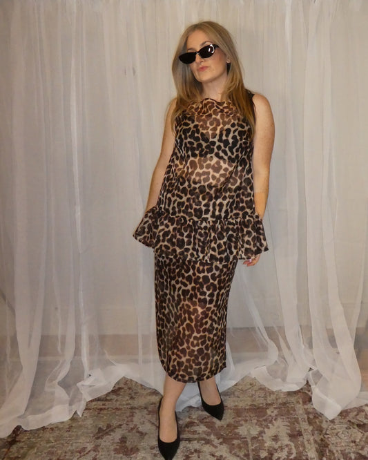 Woman wearing a leopard print dress standing in front of a white curtain.