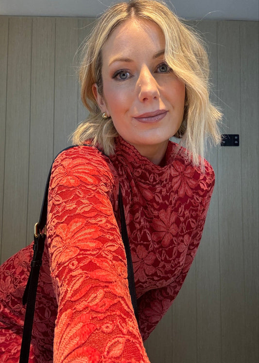 Woman wearing a red lace top against a neutral background