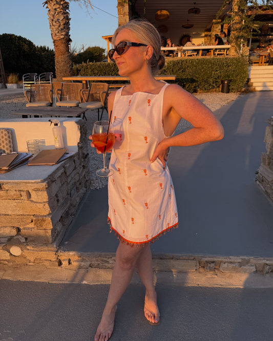 Woman in a white dress with orange patterns holding a glass of red wine outdoors.