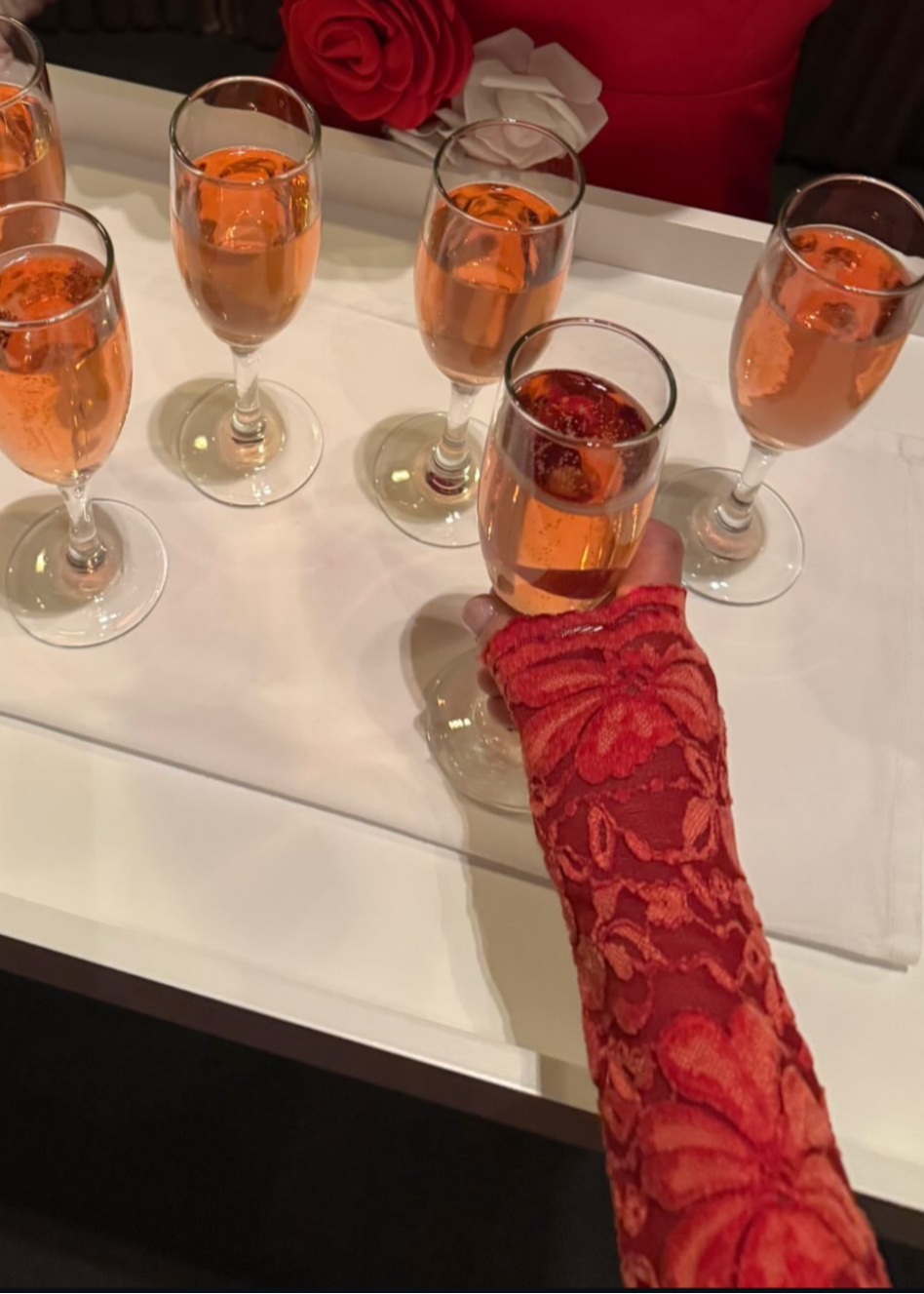 Decorative setup with red floral arrangement, white gloves, and glasses with orange liquid on a white surface.
