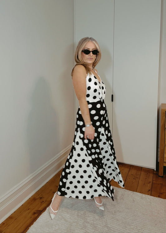 Woman in a black and white polka dot dress standing in a room with wooden flooring and a white wall.