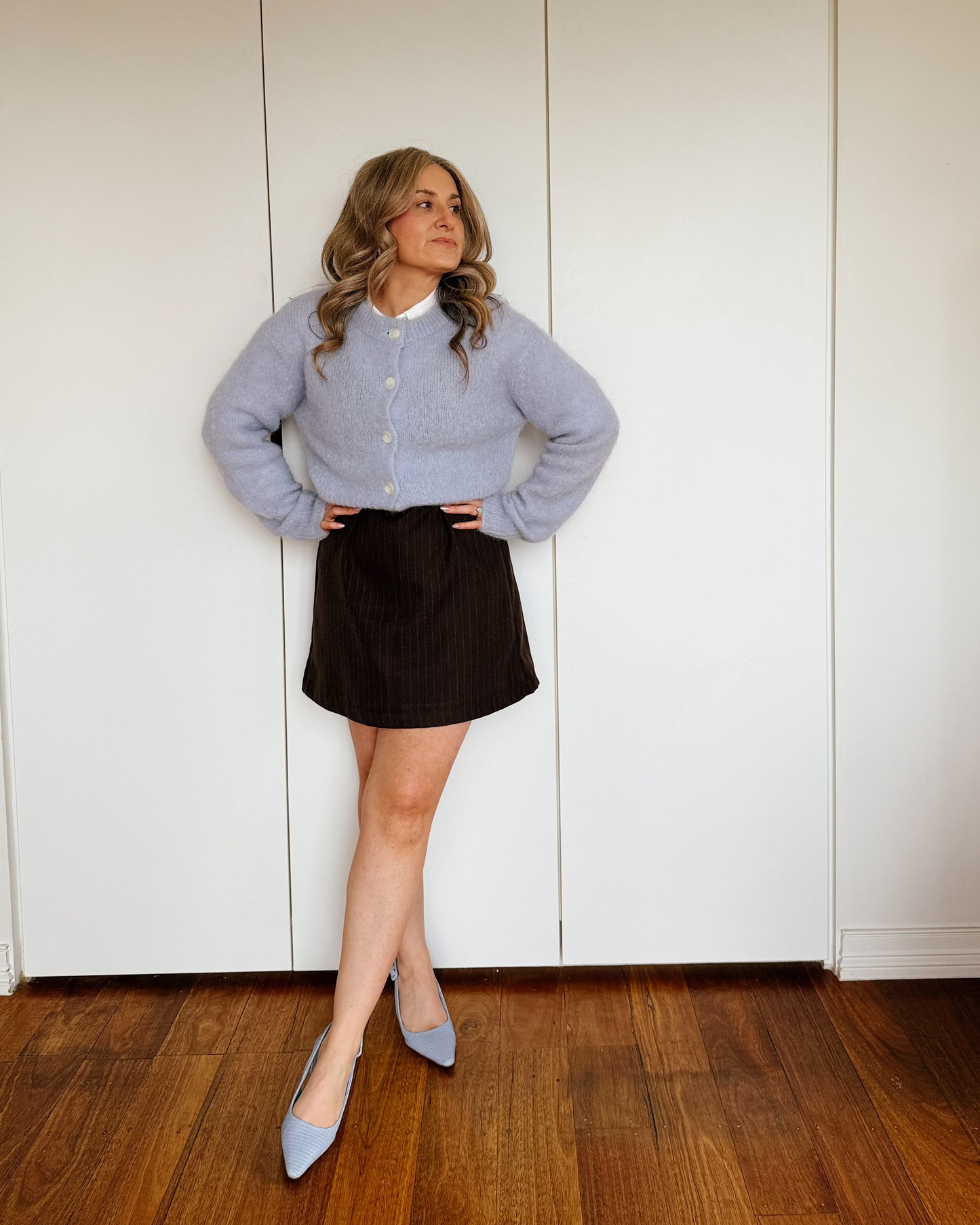 Model wearing a blue cardigan with a tailored espresso pinstripe mini dress with a fitted silhouette by By Bel.