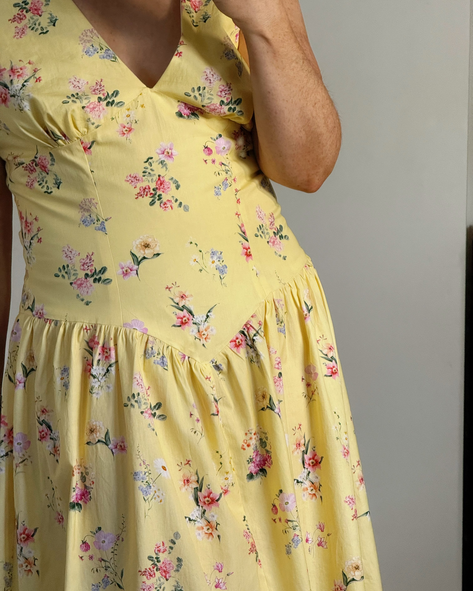 A close-up of a person wearing a yellow floral dress, showing the bodice, skirt, and part of the arm against a plain light gray background.