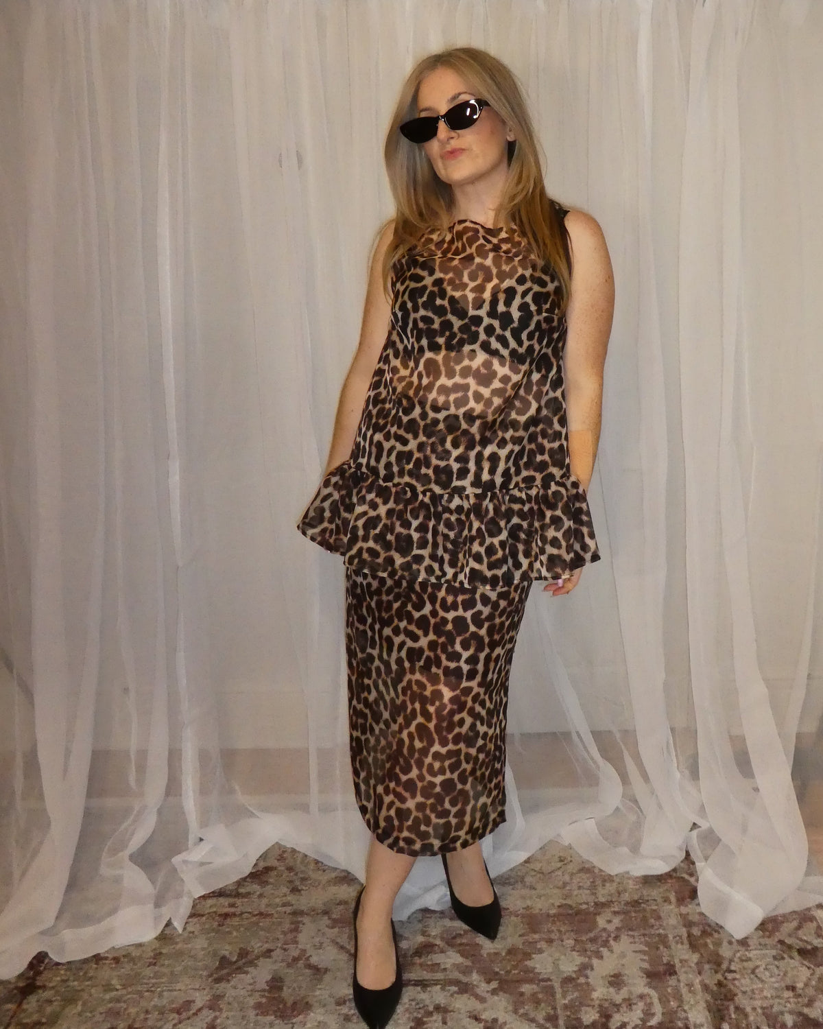Woman wearing a leopard print dress standing in front of a white curtain.