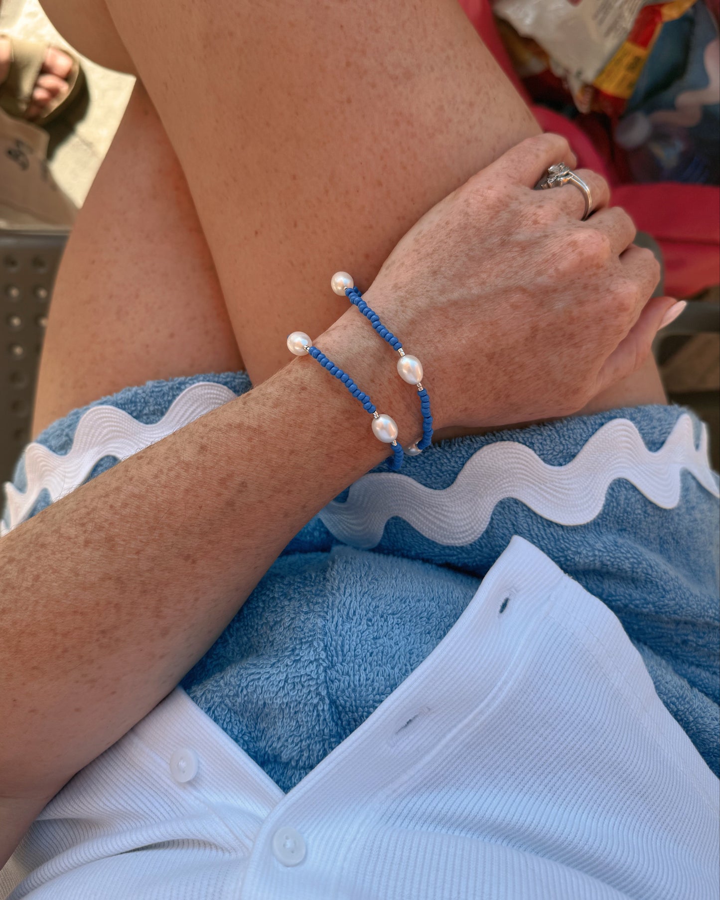 Person wearing a blue bracelet with white beads on a beach chair.