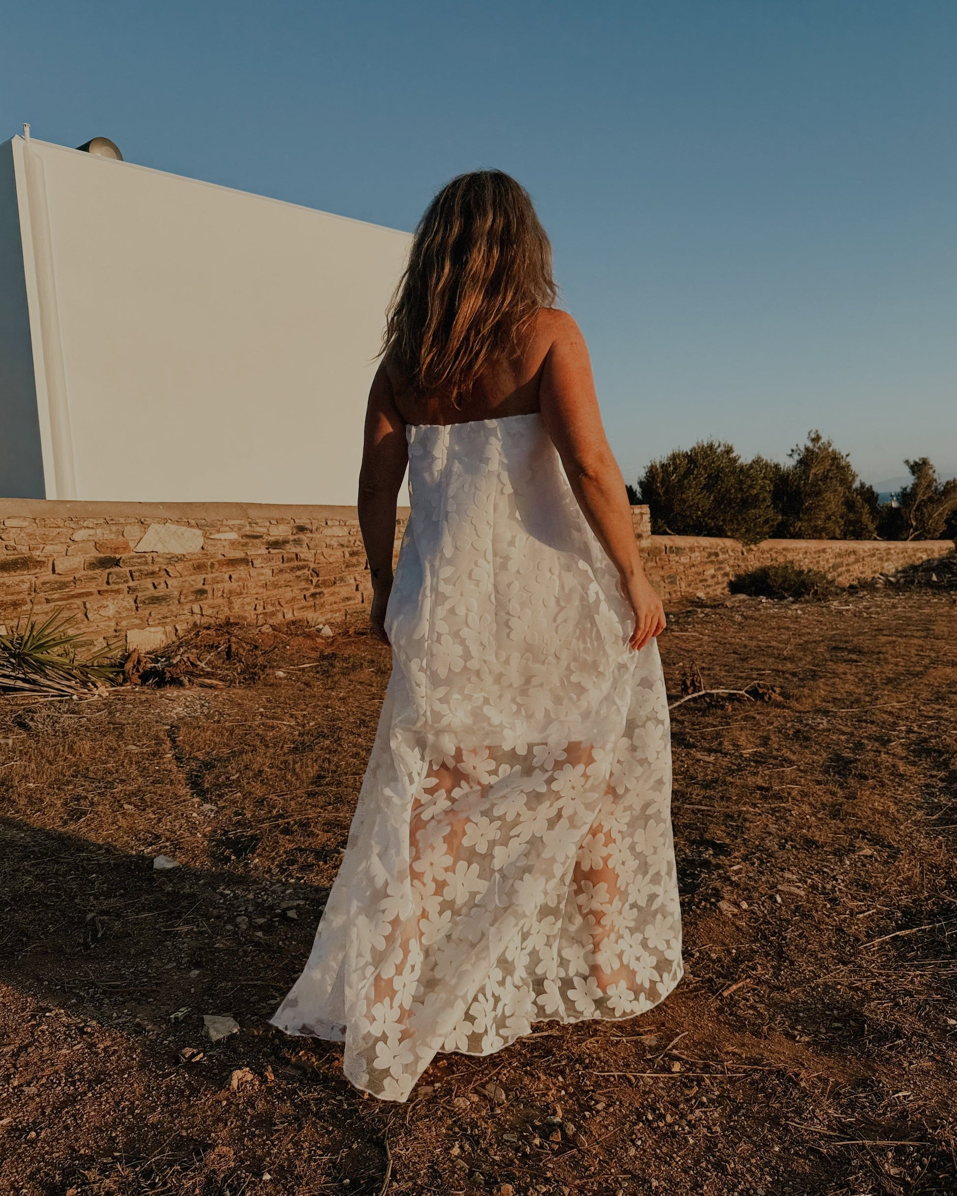 Woman in a white dress standing in a desert-like landscape with a clear blue sky.