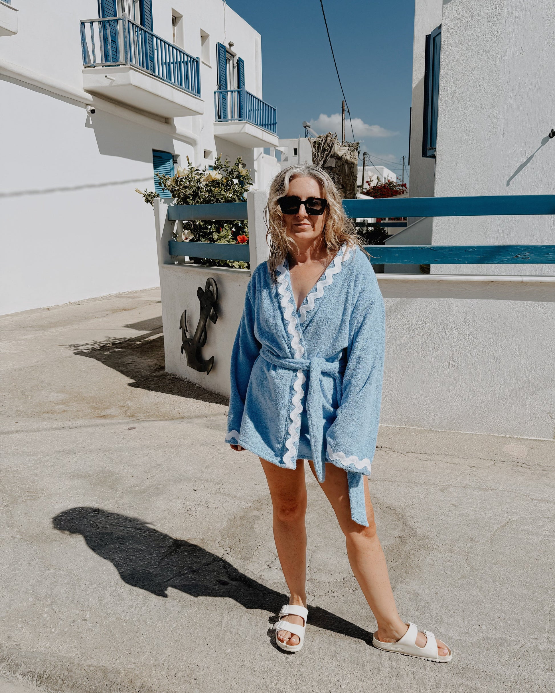 Woman in a blue robe standing in front of white buildings with blue accents on a sunny day.