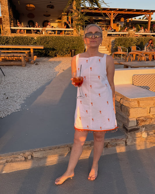 Woman in a white dress holding a drink outdoors at sunset