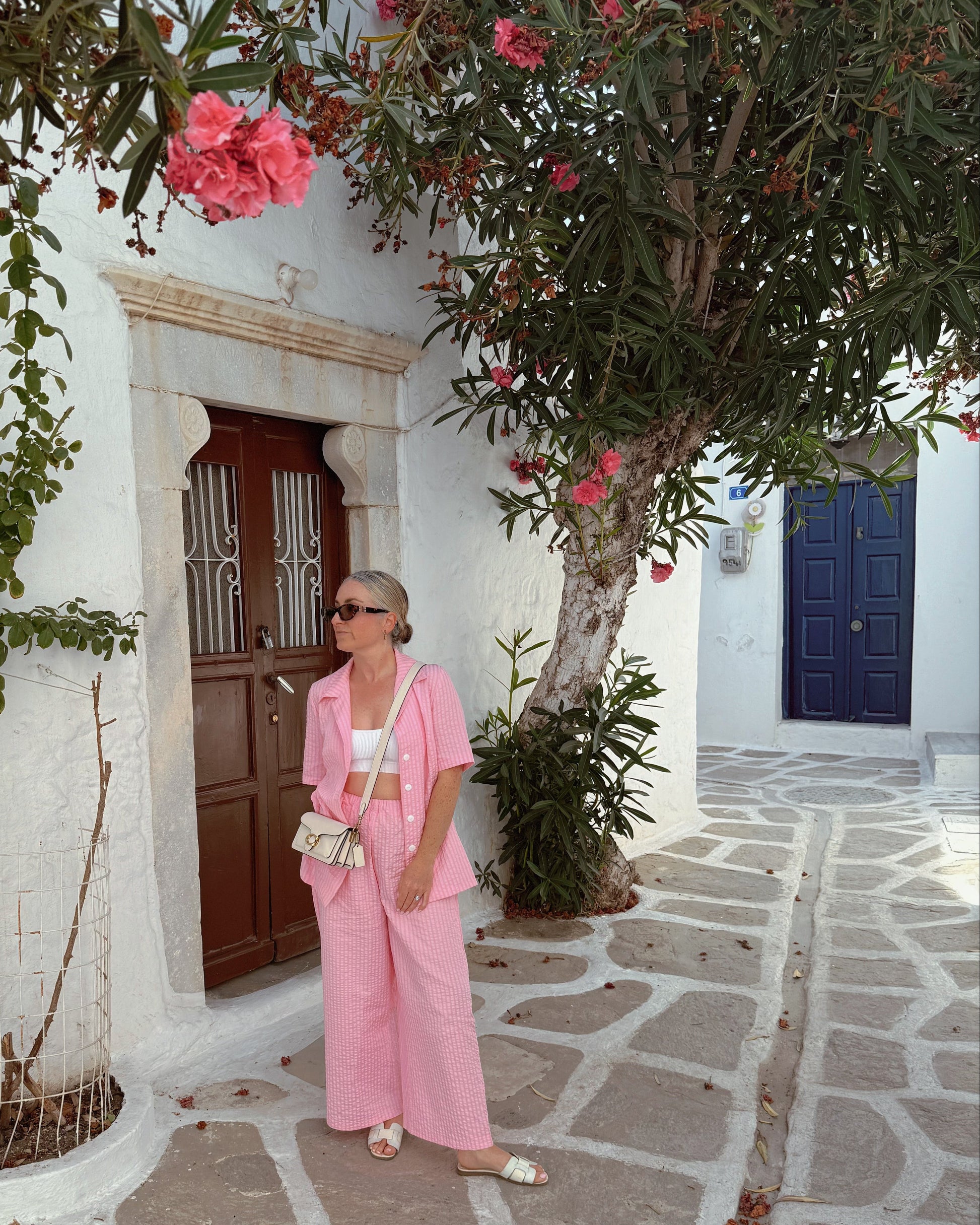 Woman in a pink outfit standing in front of a white building with a tree and flowers.