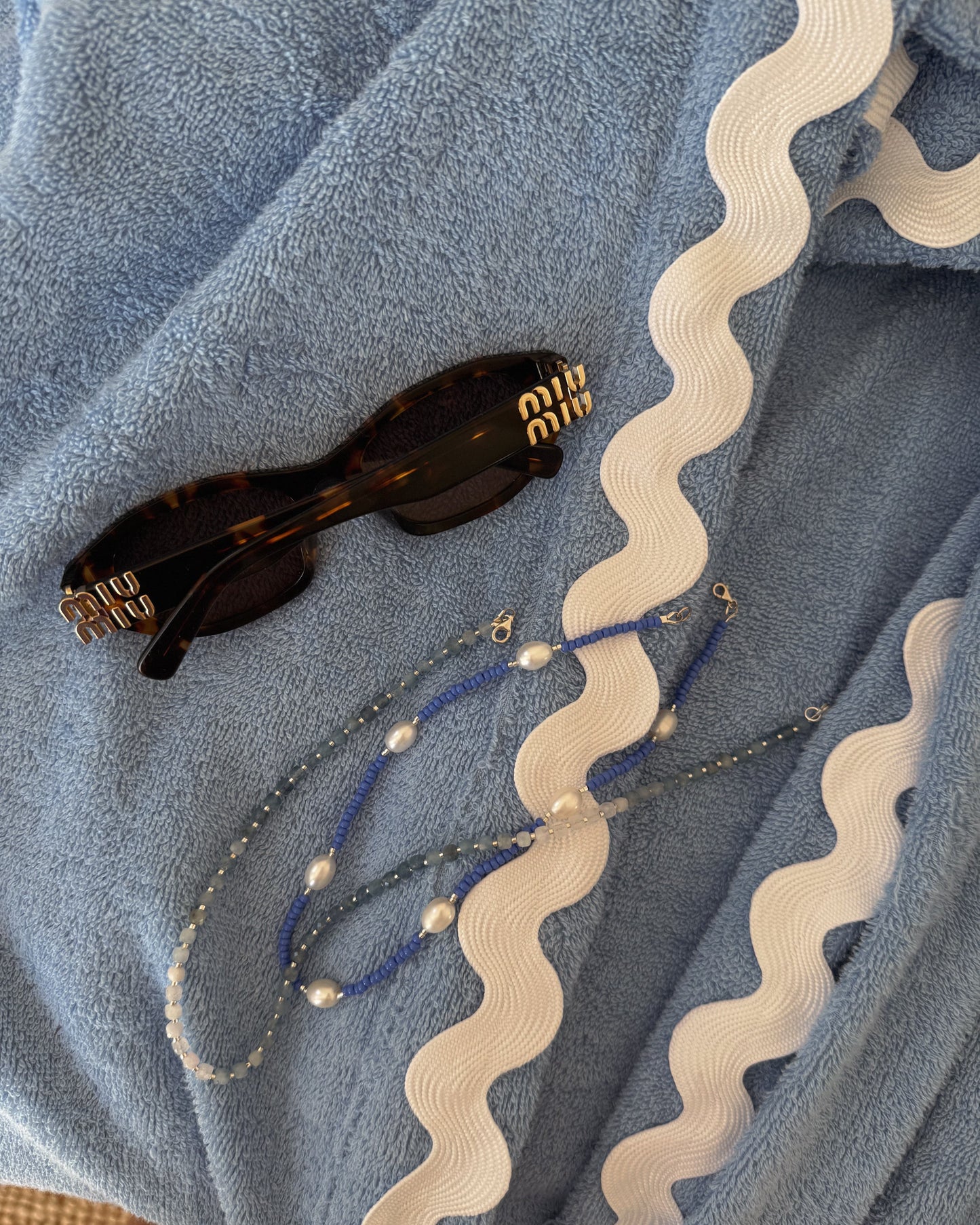 Sunglasses and beaded necklaces on a textured blue fabric background