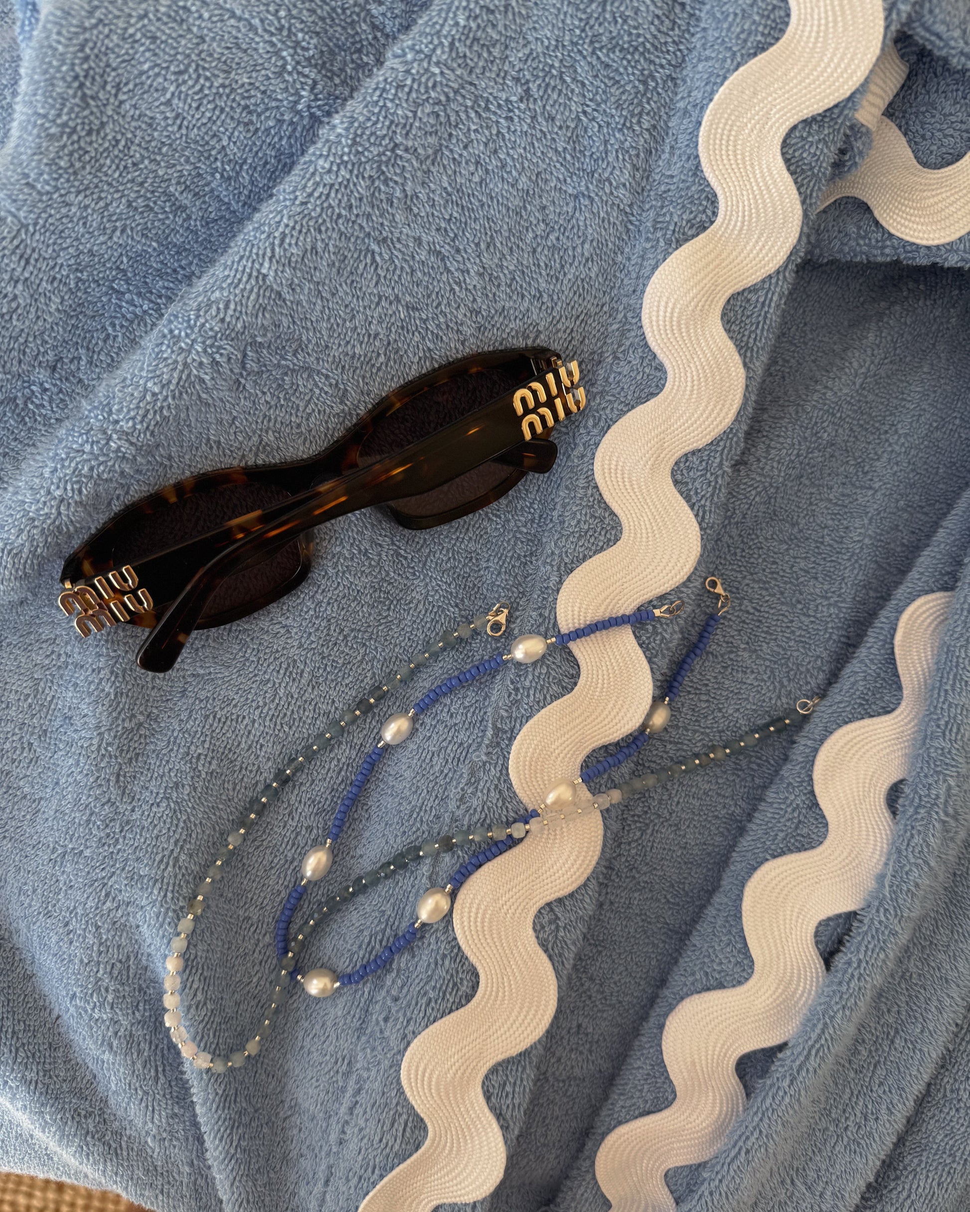 Sunglasses and beaded necklaces on a textured blue fabric background