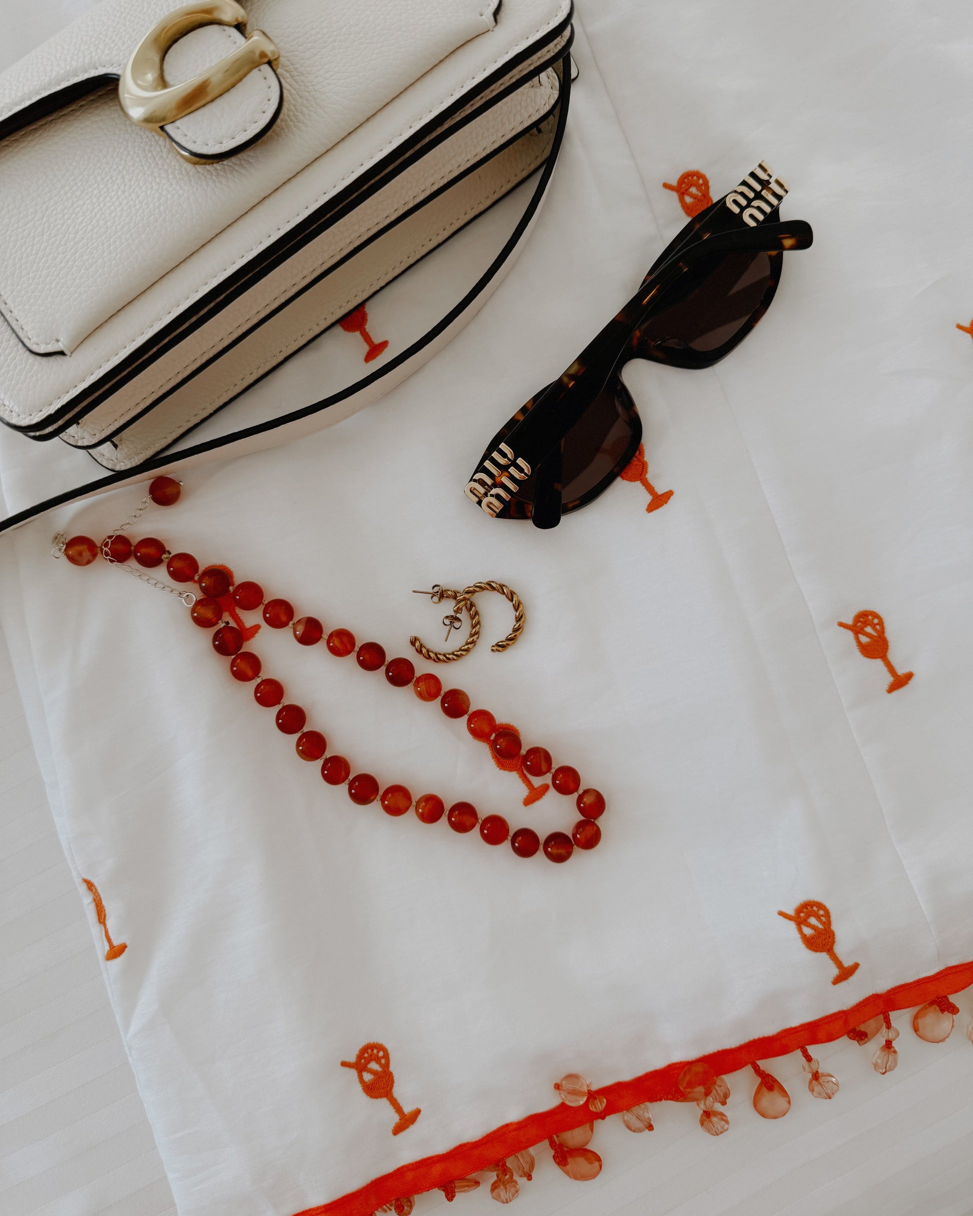 White handbag with sunglasses and red beads on a white fabric background