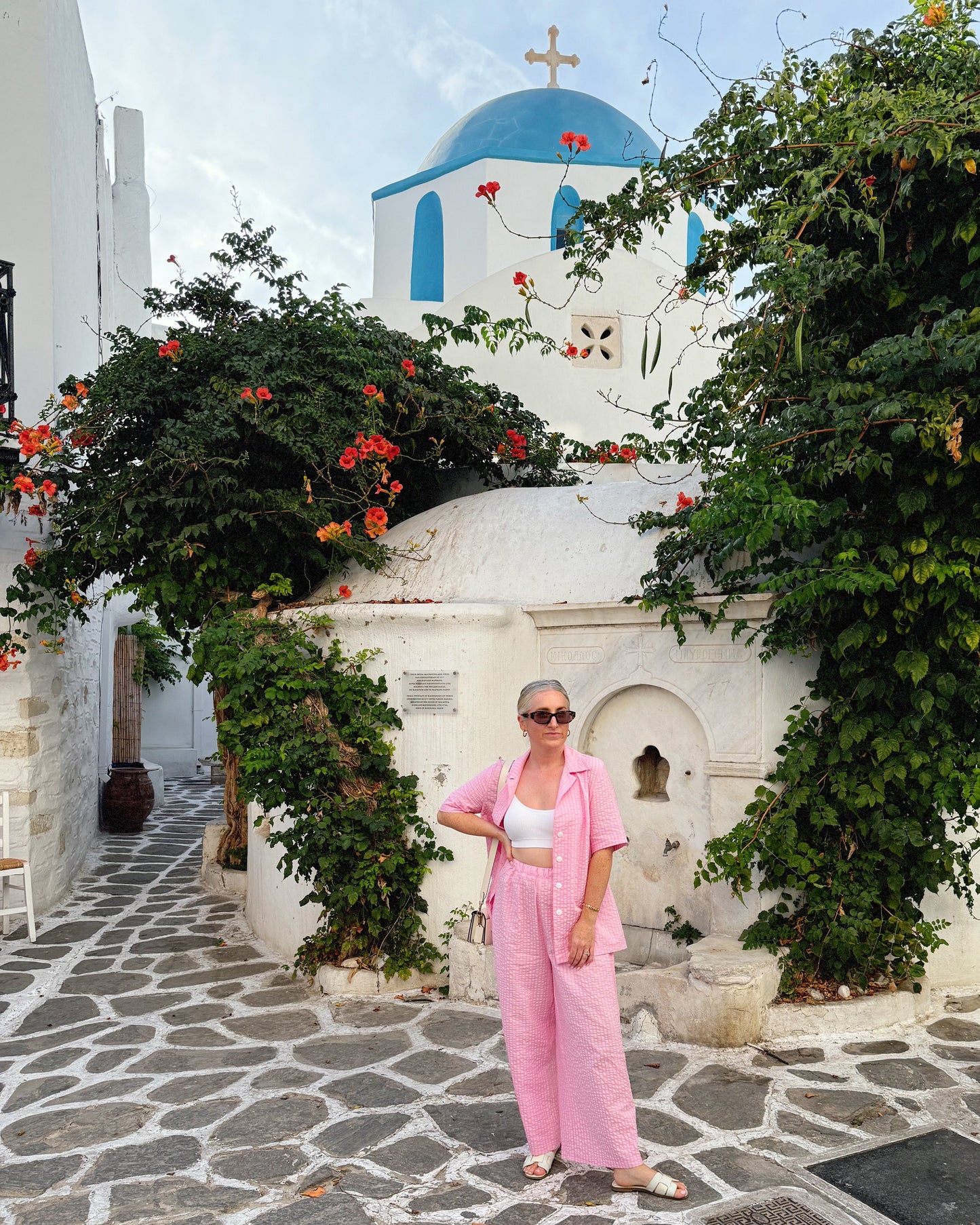 Woman in a pink outfit standing in front of a white building with a blue dome in a Mediterranean setting.