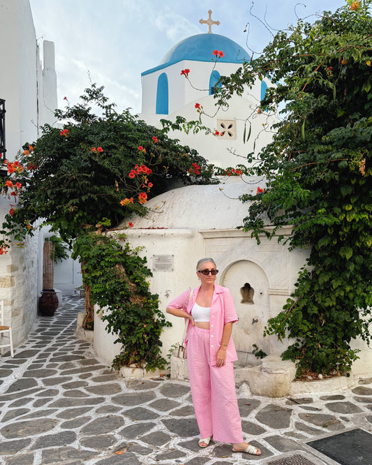 Woman in a pink outfit standing in front of a white building with a blue dome in a Mediterranean setting.