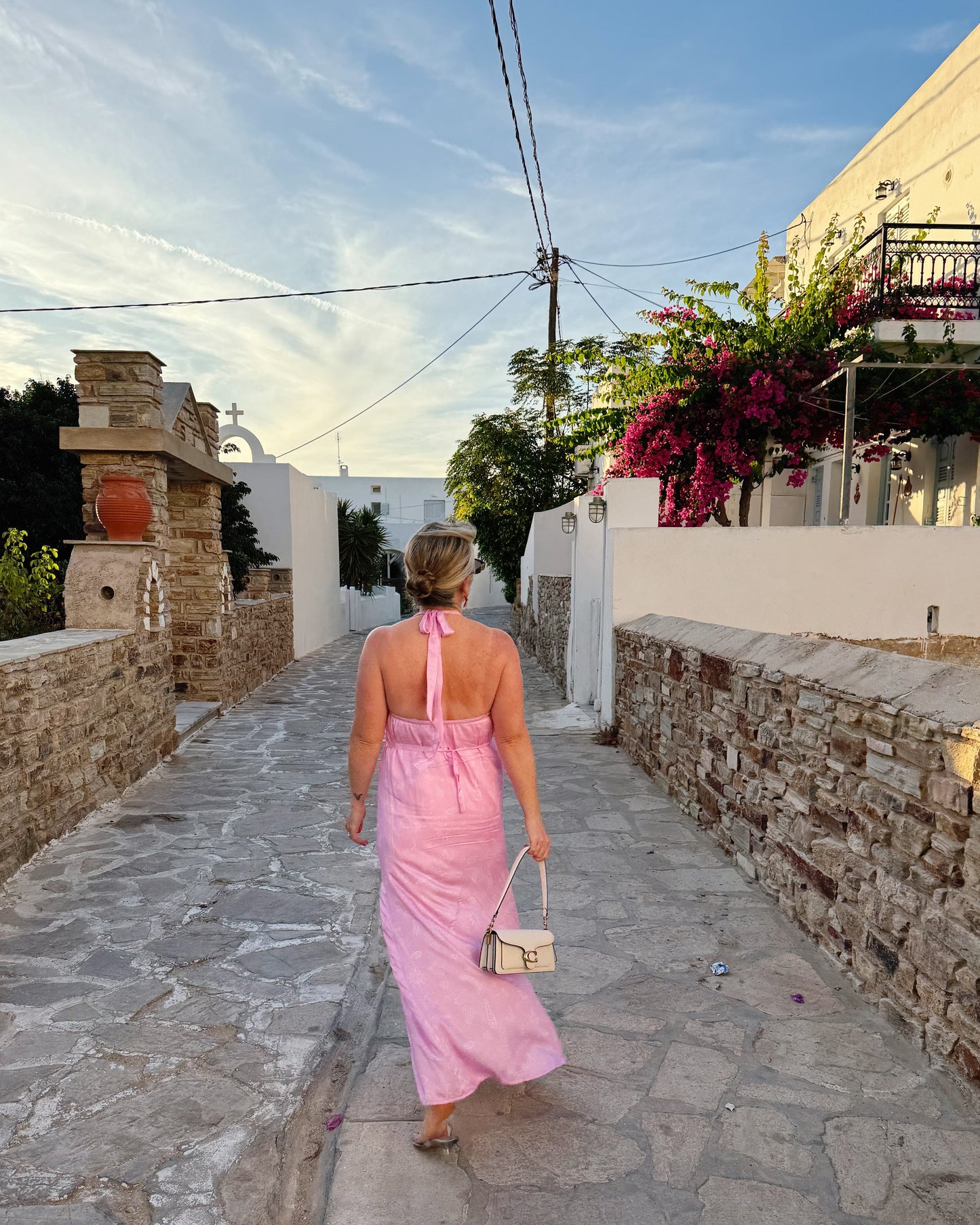 Woman in a pink dress walking down a stone-paved street in a Mediterranean village.