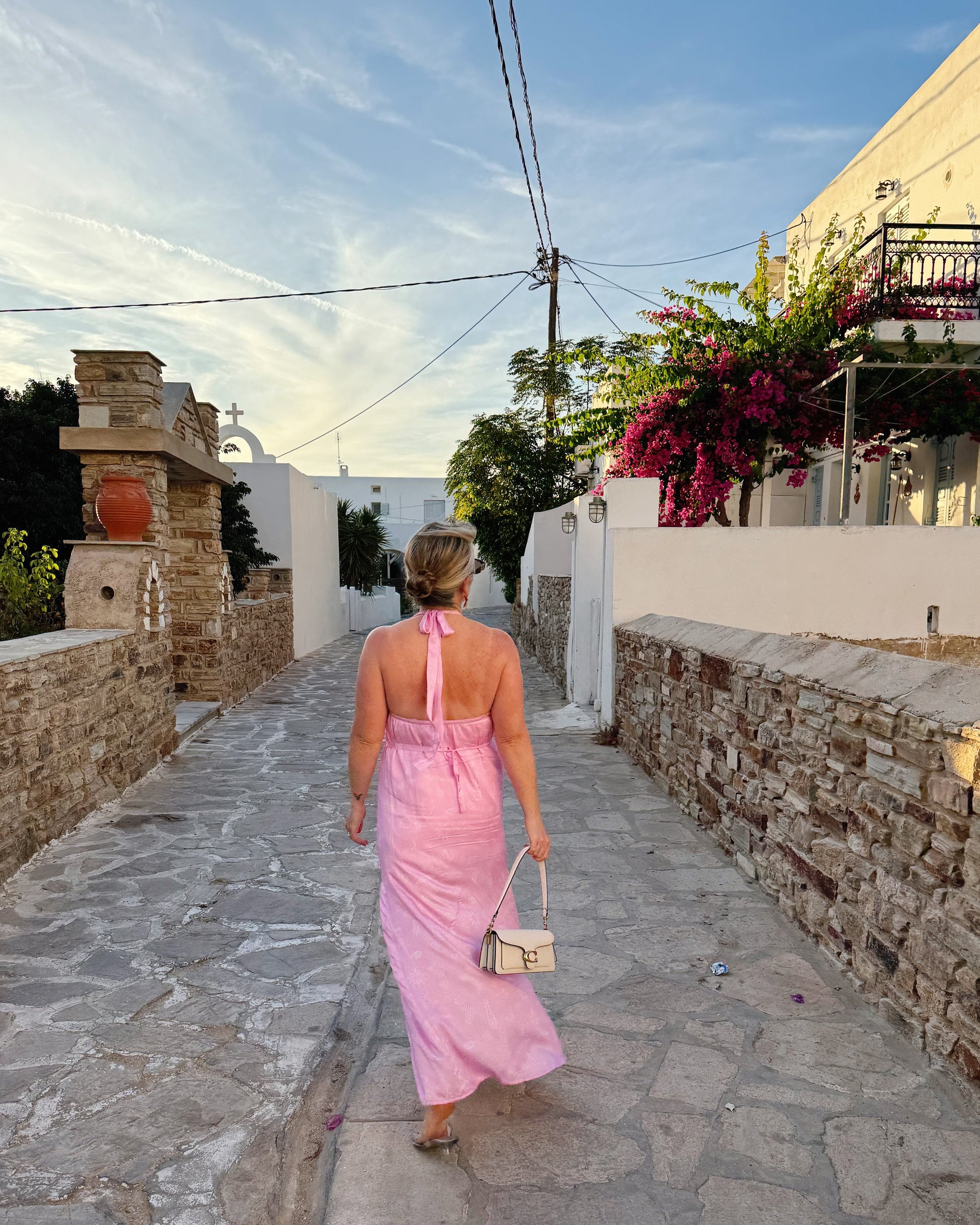 Woman in a pink dress walking down a stone-paved street in a Mediterranean village.