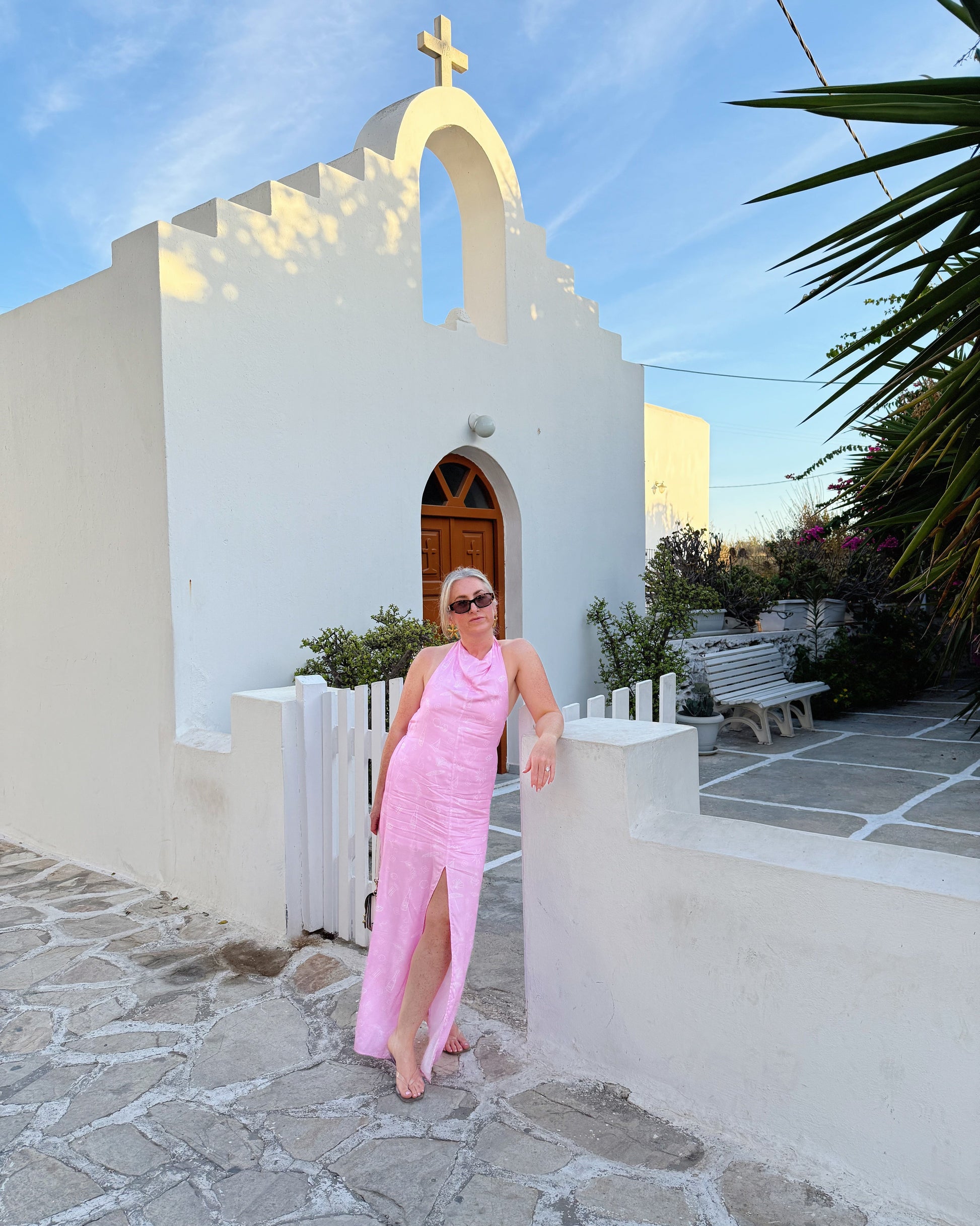 Woman in a pink dress standing in front of a white church with a blue sky.