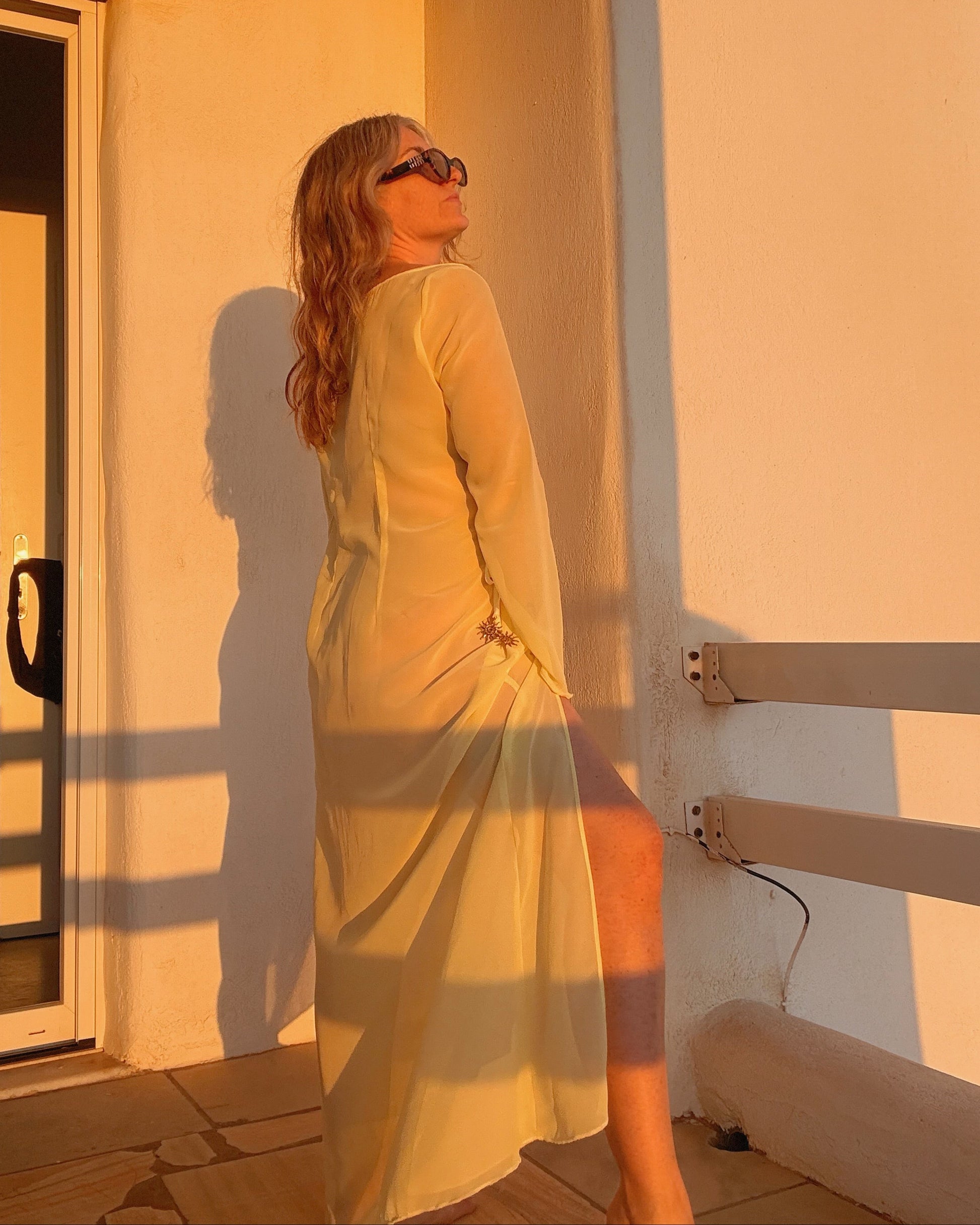 Woman in a yellow dress standing in a sunlit room casting a shadow on the wall.