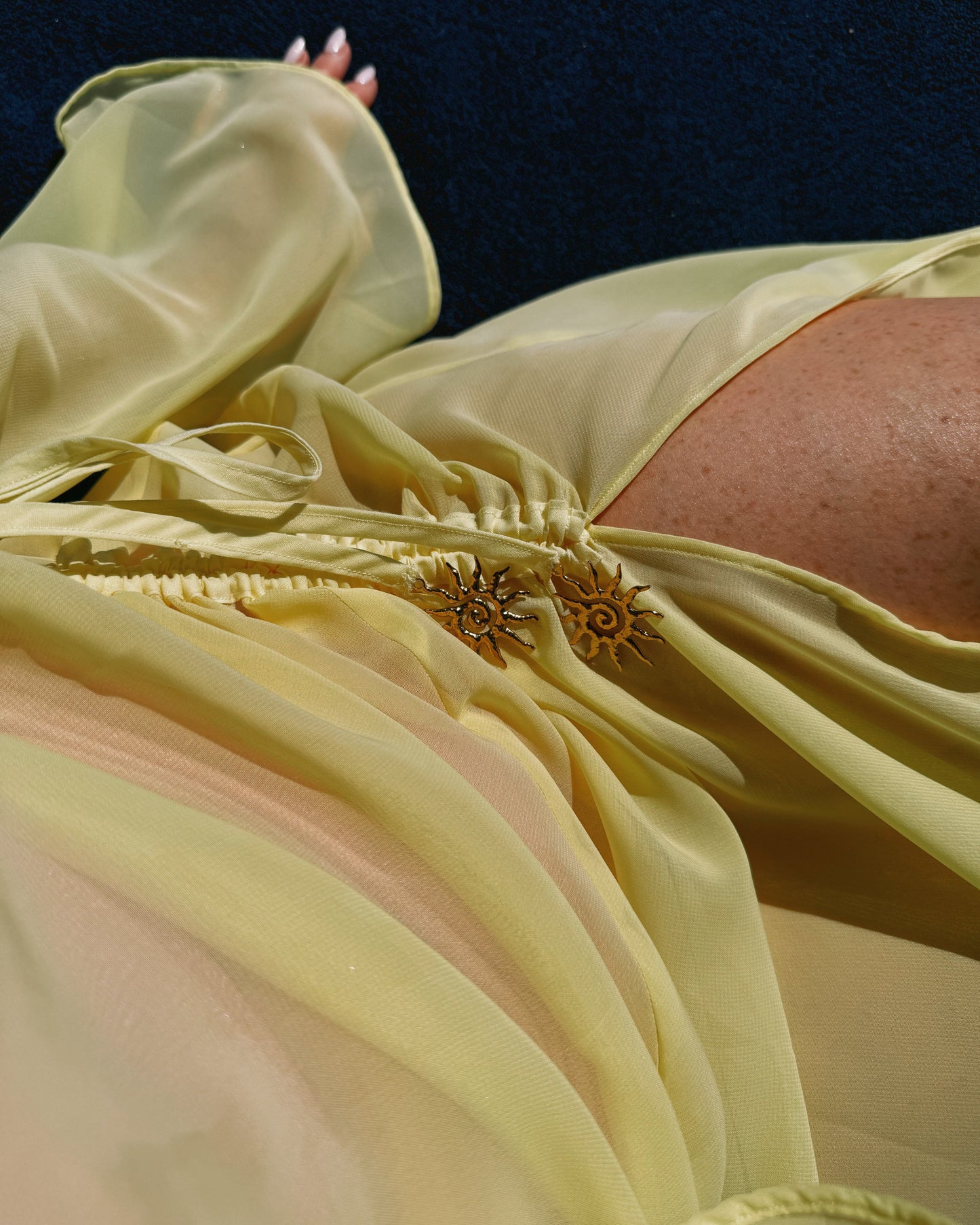 Close-up of a person wearing a light yellow dress with floral details against a dark background