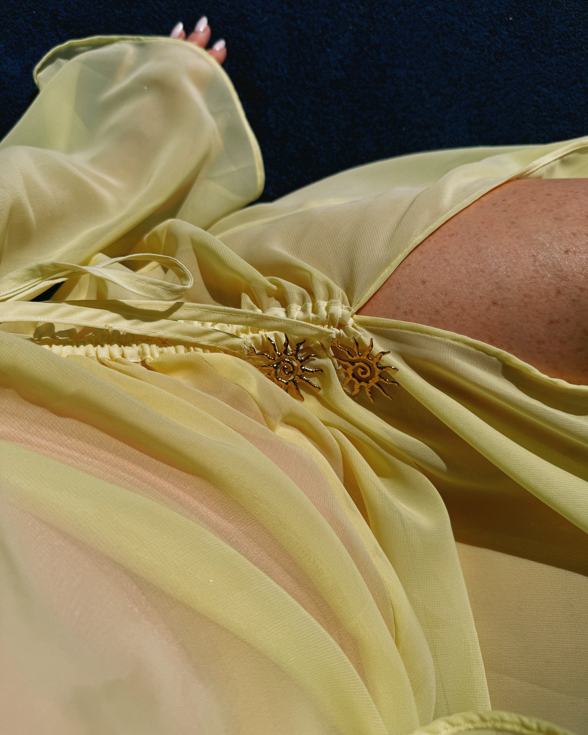 Close-up of a person wearing a light yellow dress with floral details against a dark background