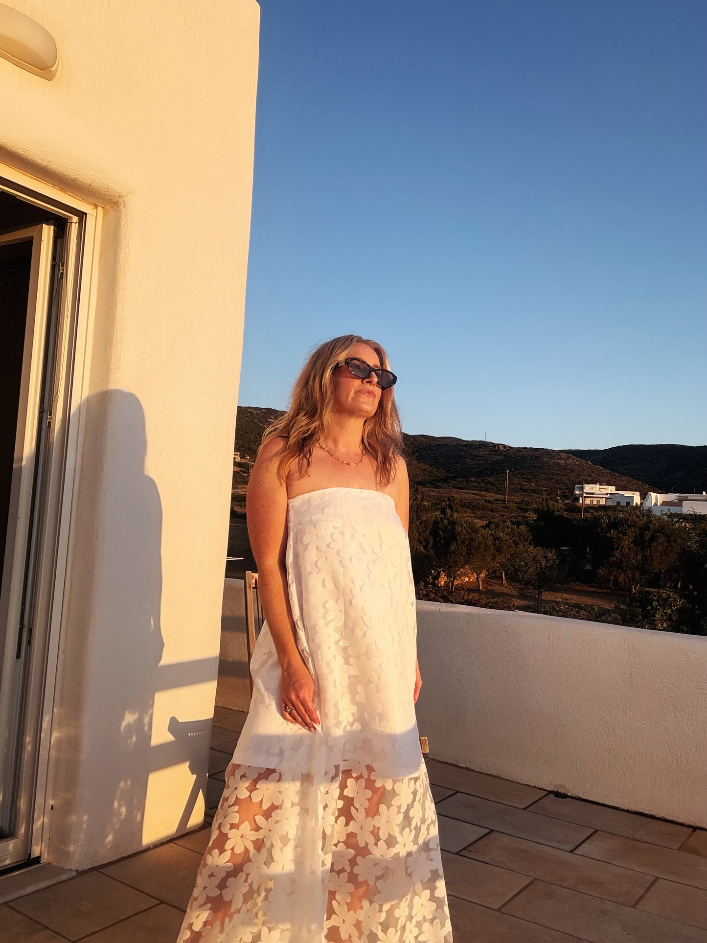 Woman in a white dress standing on a balcony with a scenic view