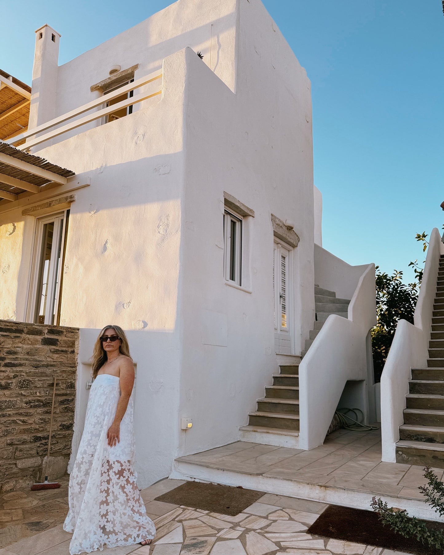 Woman in a white dress standing in front of a white building with stone steps.