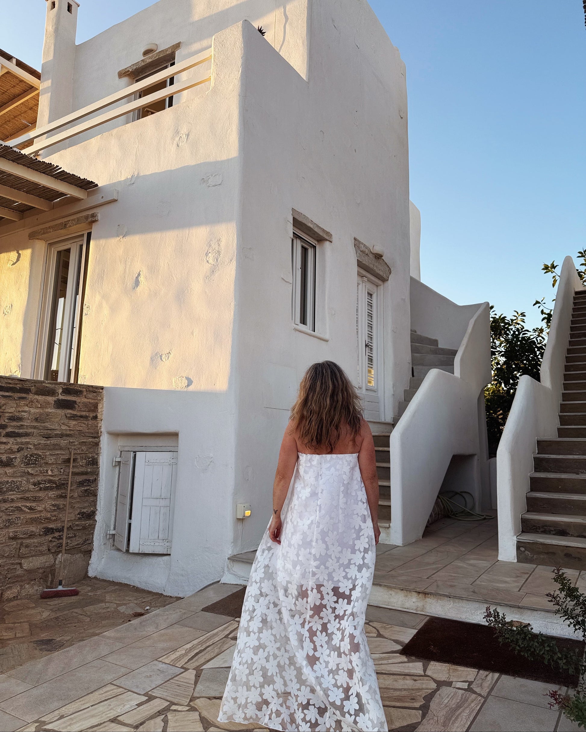Woman in a white dress standing in front of a white architectural structure with a clear blue sky.