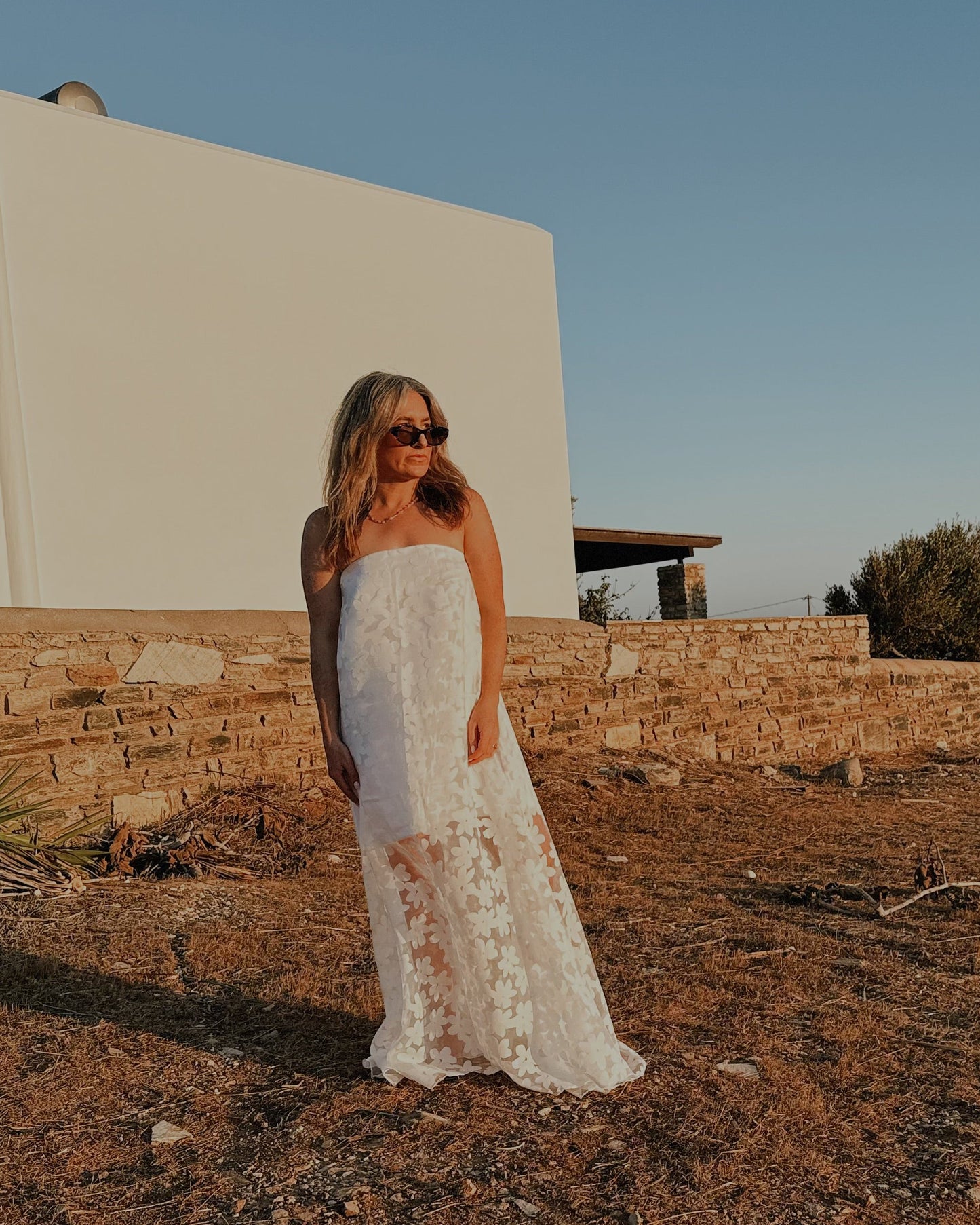 Woman in a white dress standing in a desert-like landscape with a clear blue sky.
