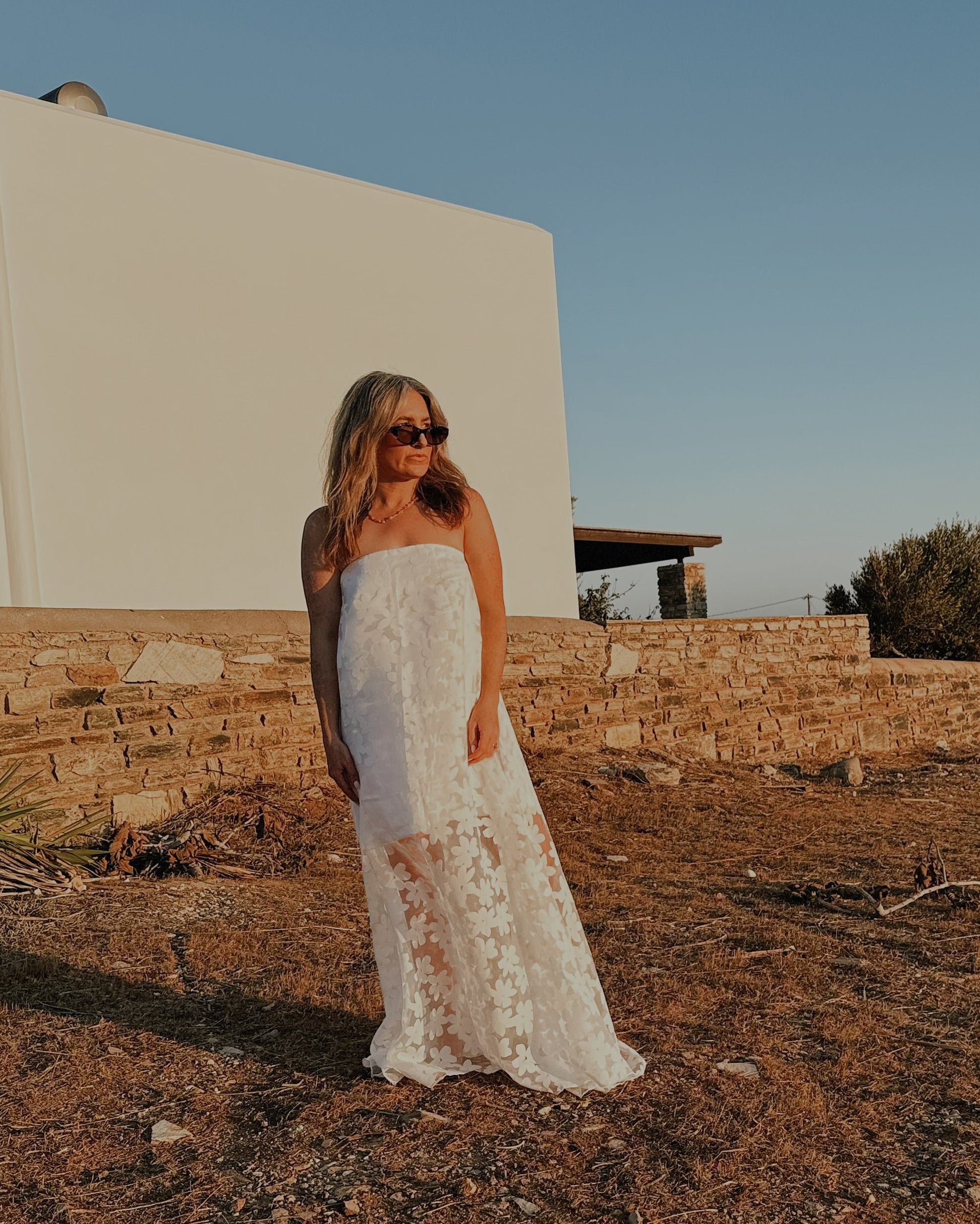 Woman in a white dress standing in a desert-like landscape with a clear blue sky.