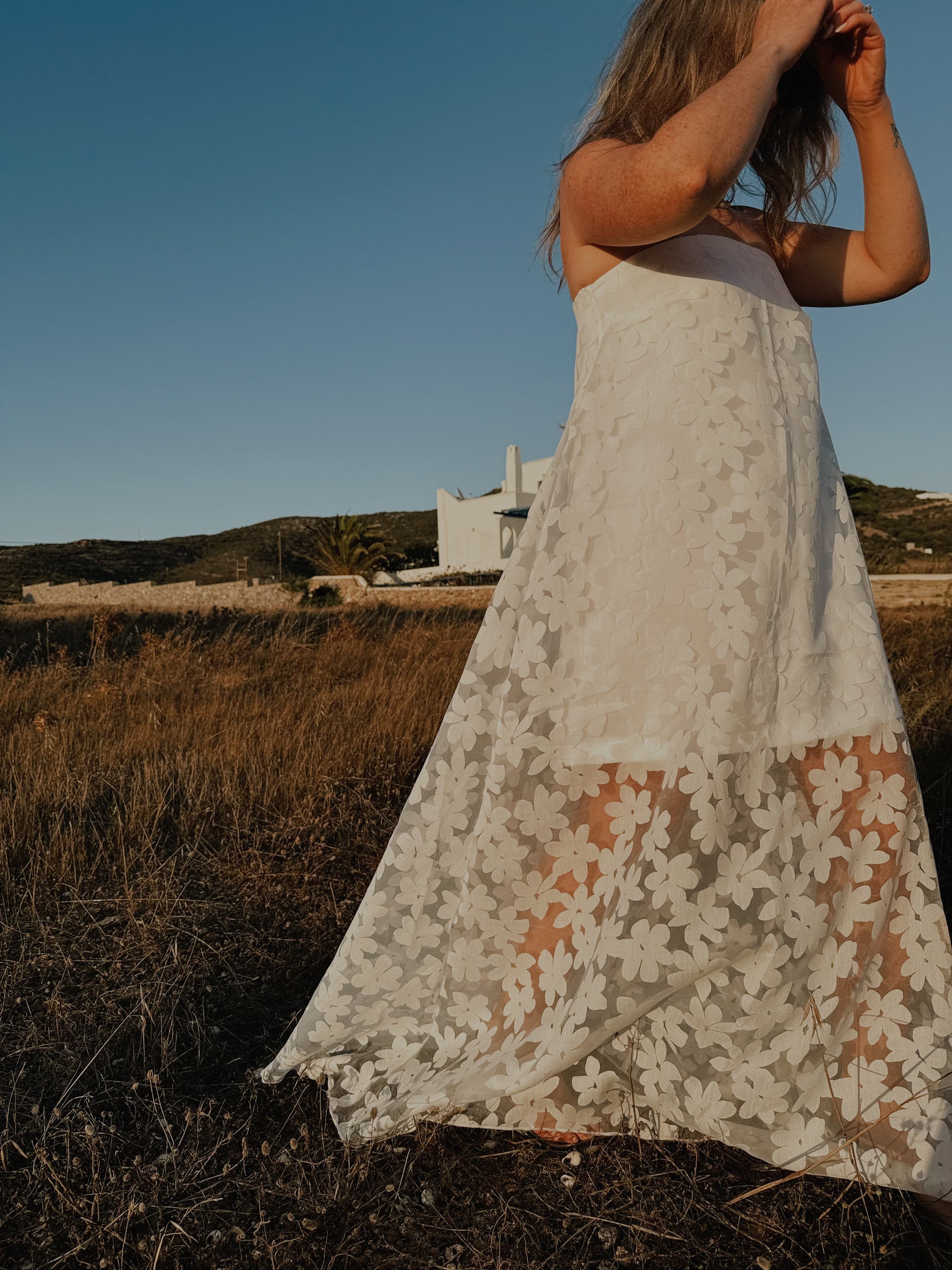Person wearing a white lace dress standing in a field with a clear blue sky.