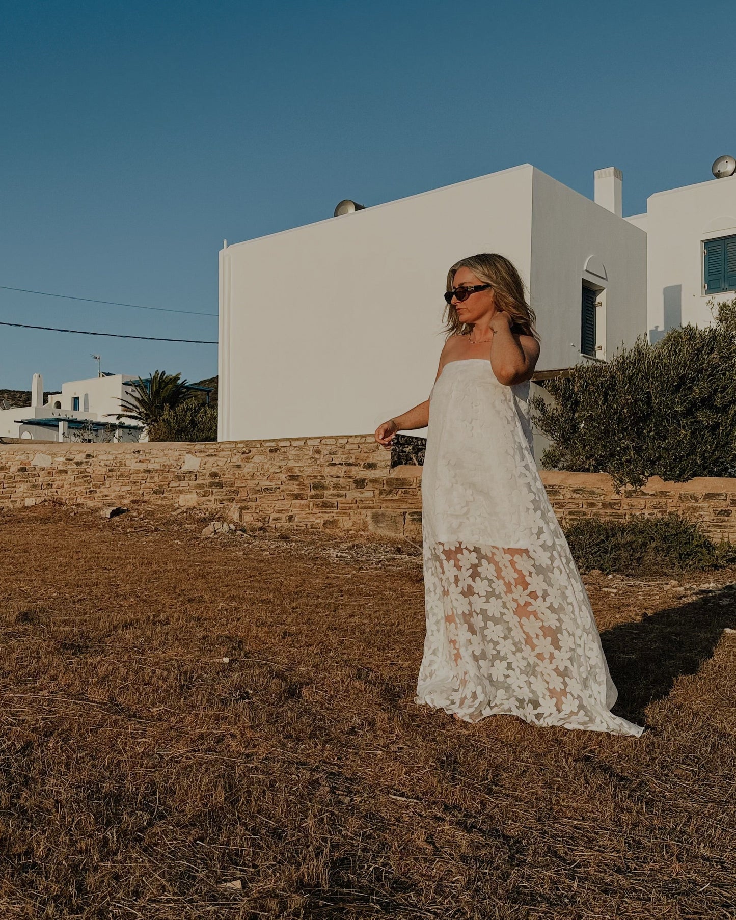 Woman in a white dress standing in a sunlit outdoor setting with a clear blue sky.