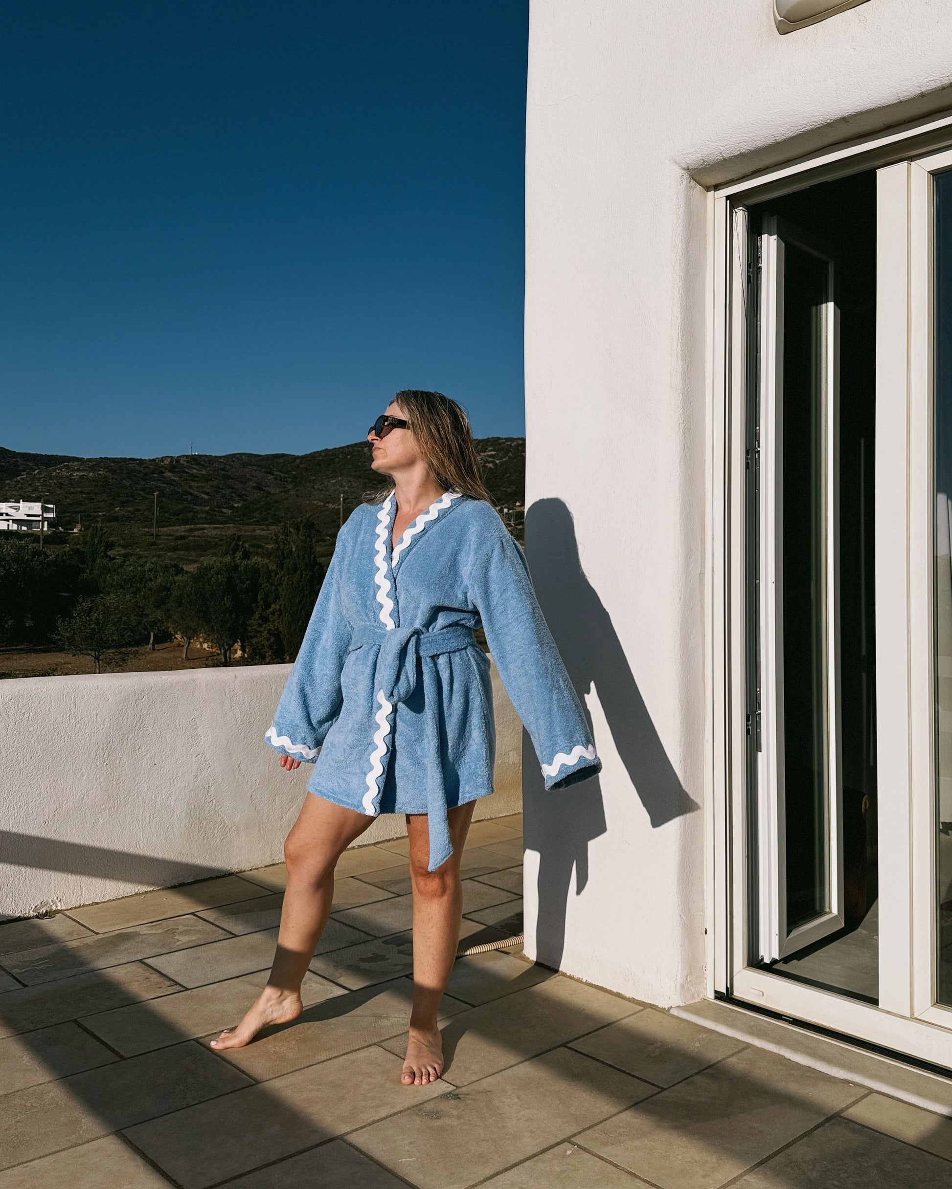 Woman in a blue robe standing on a rooftop with a scenic view