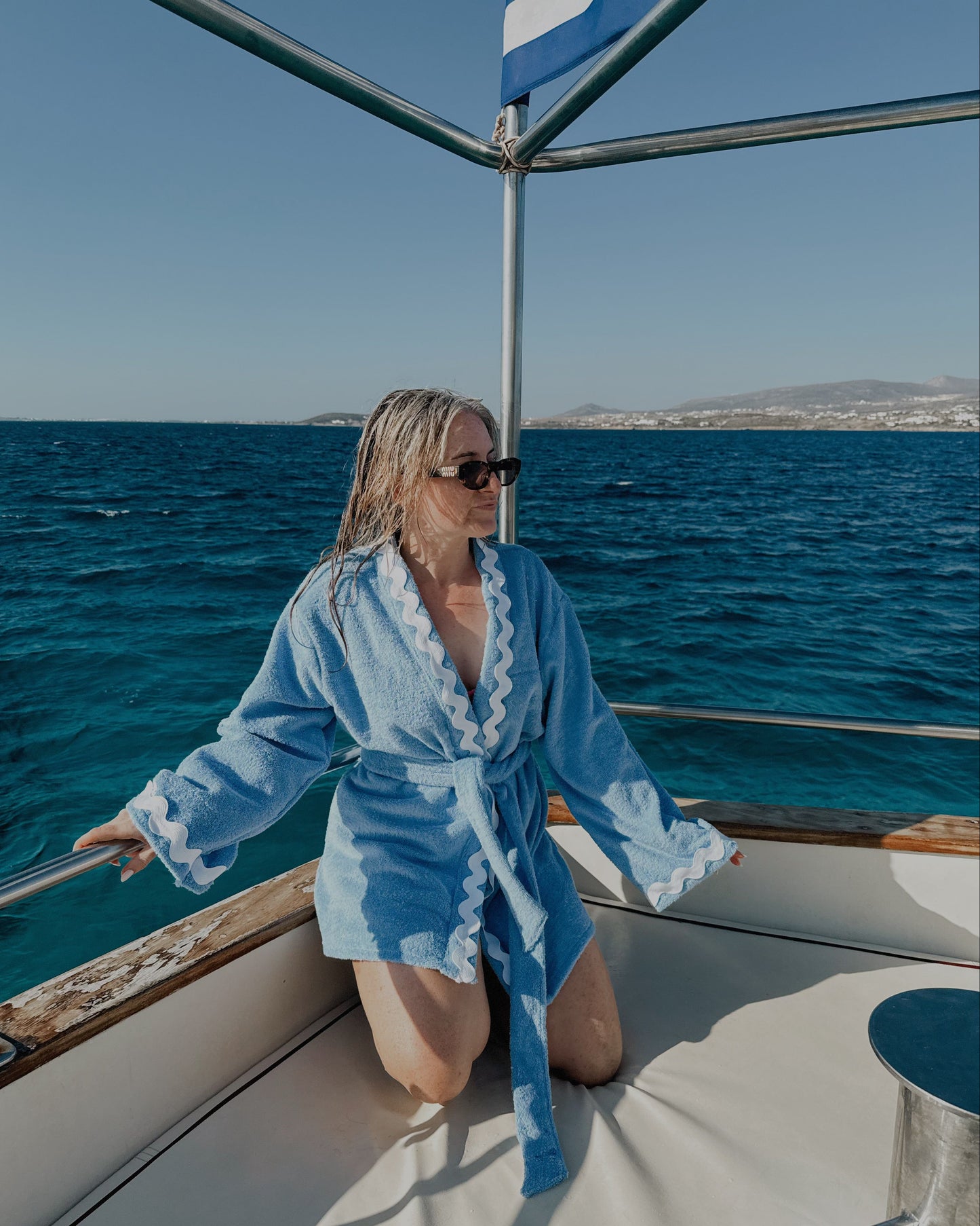 Woman in a blue robe on a boat with ocean and sky in the background