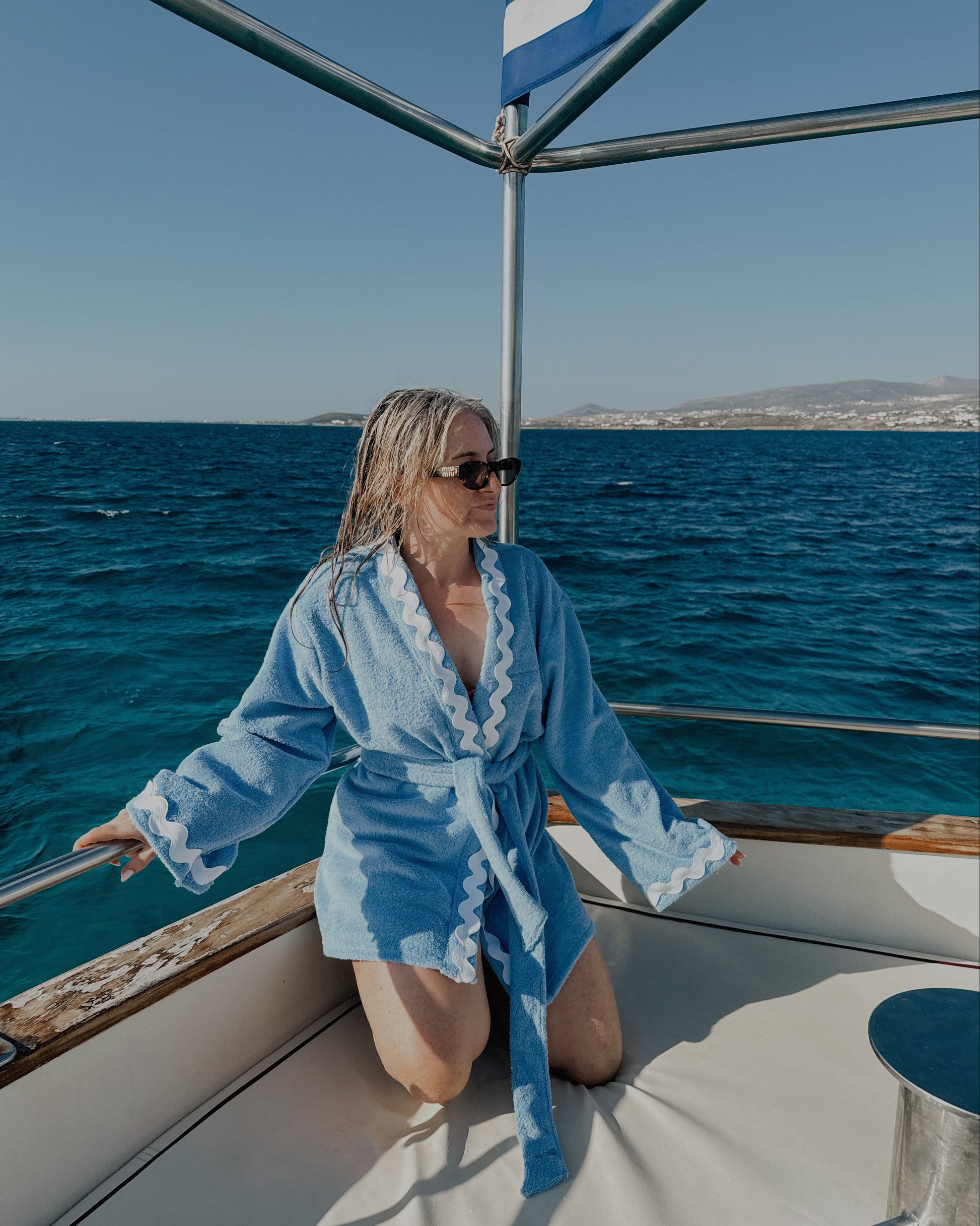 Woman in a blue robe on a boat with ocean and sky in the background
