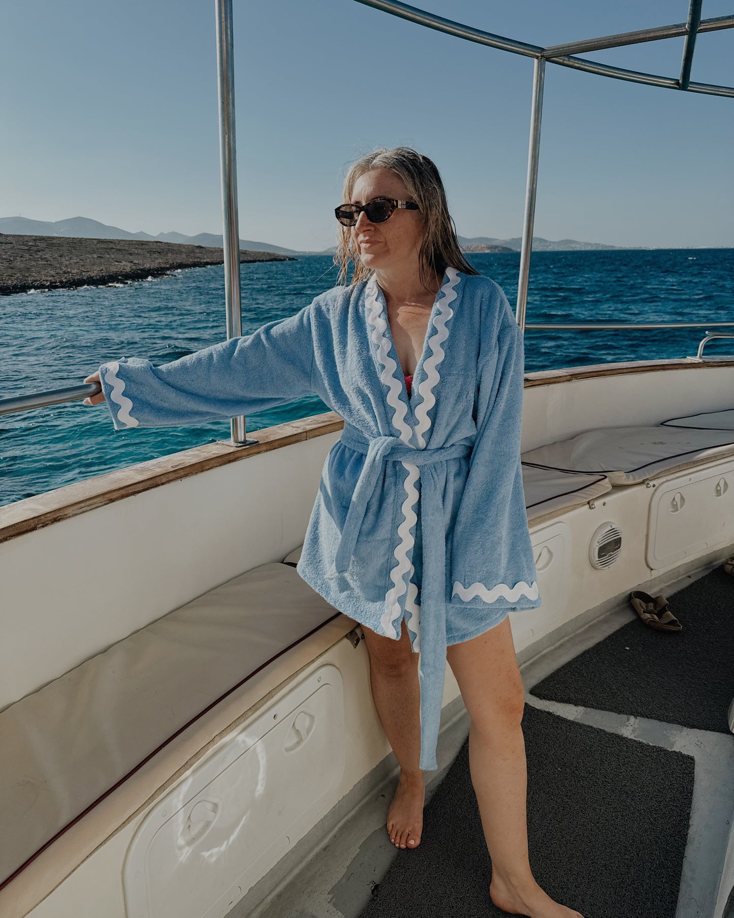 Woman in a blue robe standing on a boat with ocean view