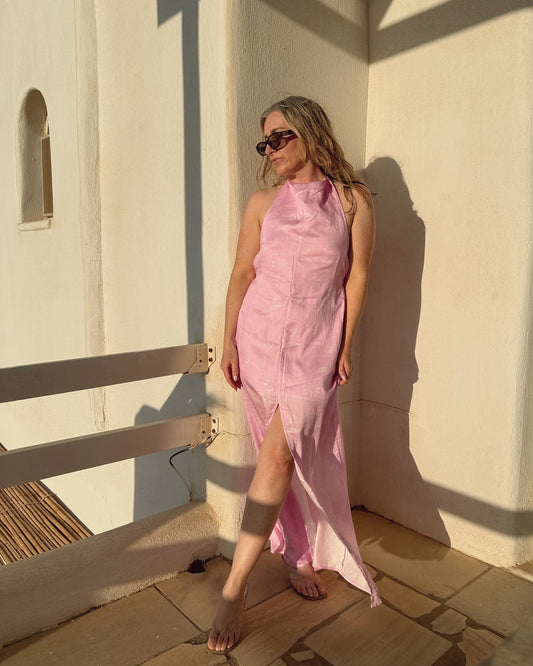 Woman in a pink dress standing against a white wall with sunlight casting shadows.