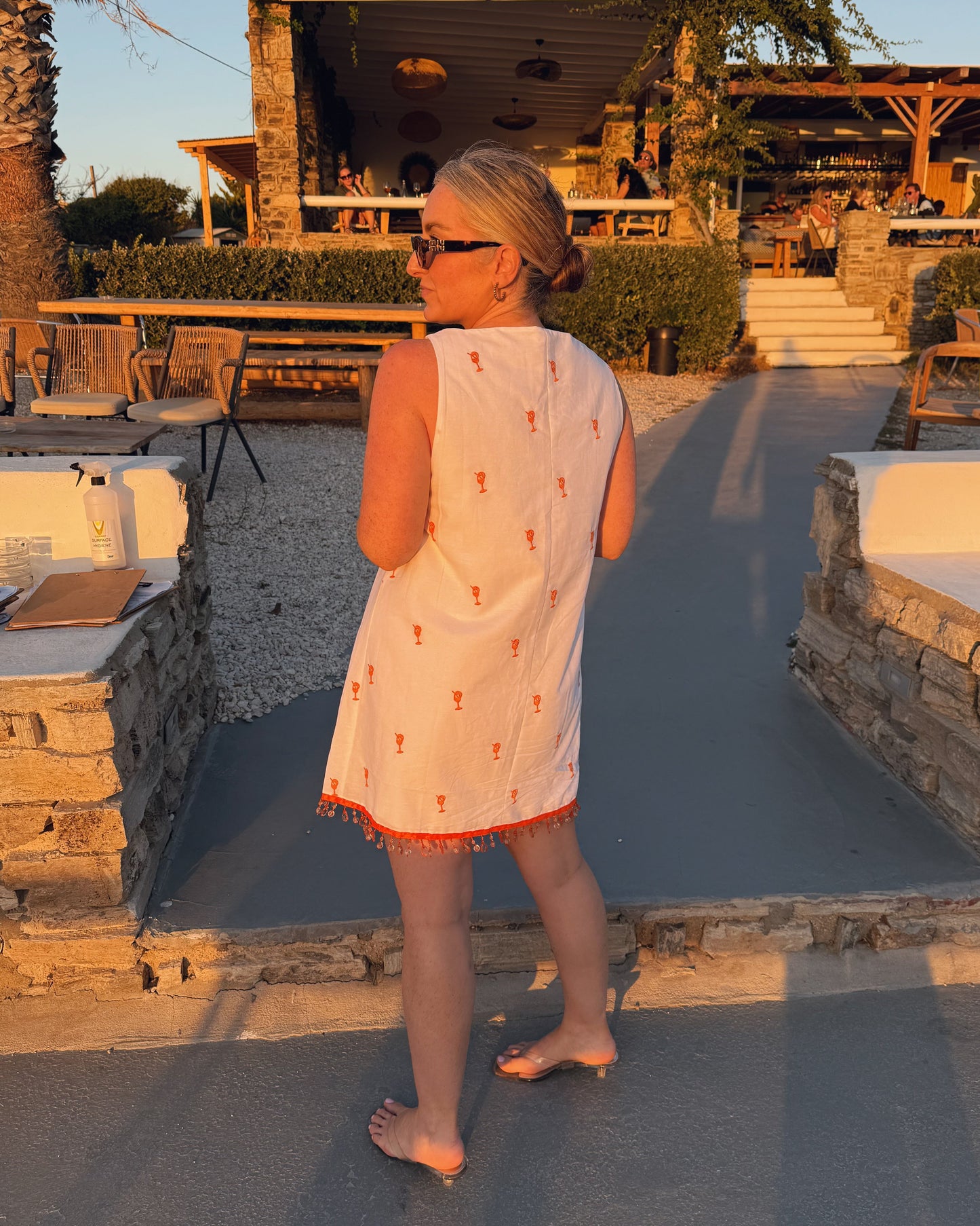 Woman in a white dress standing on a patio with outdoor furniture and a building in the background.