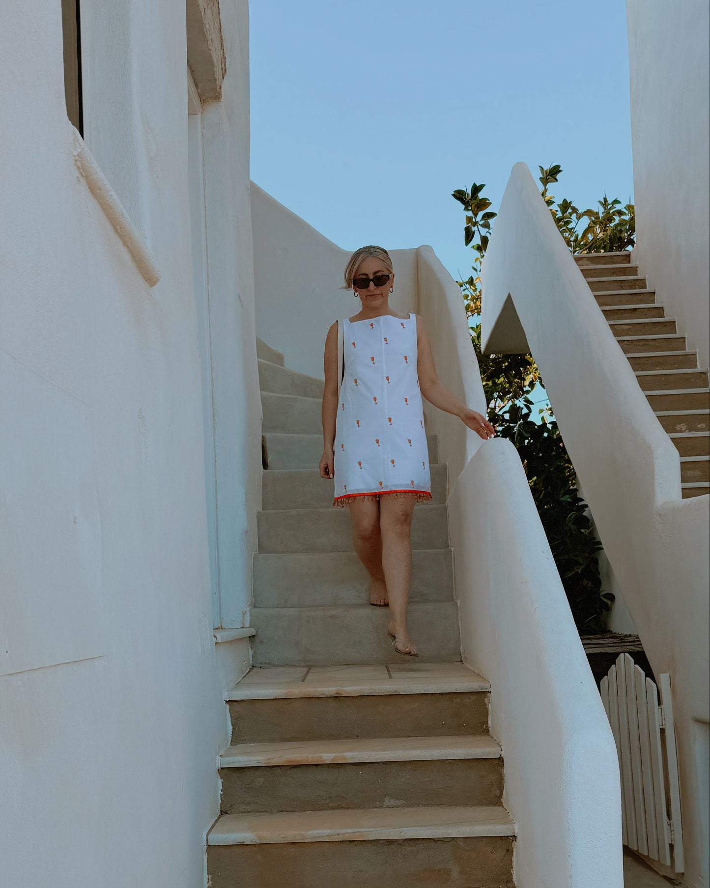 Woman in a white dress walking up a set of stairs in a sunlit outdoor setting.