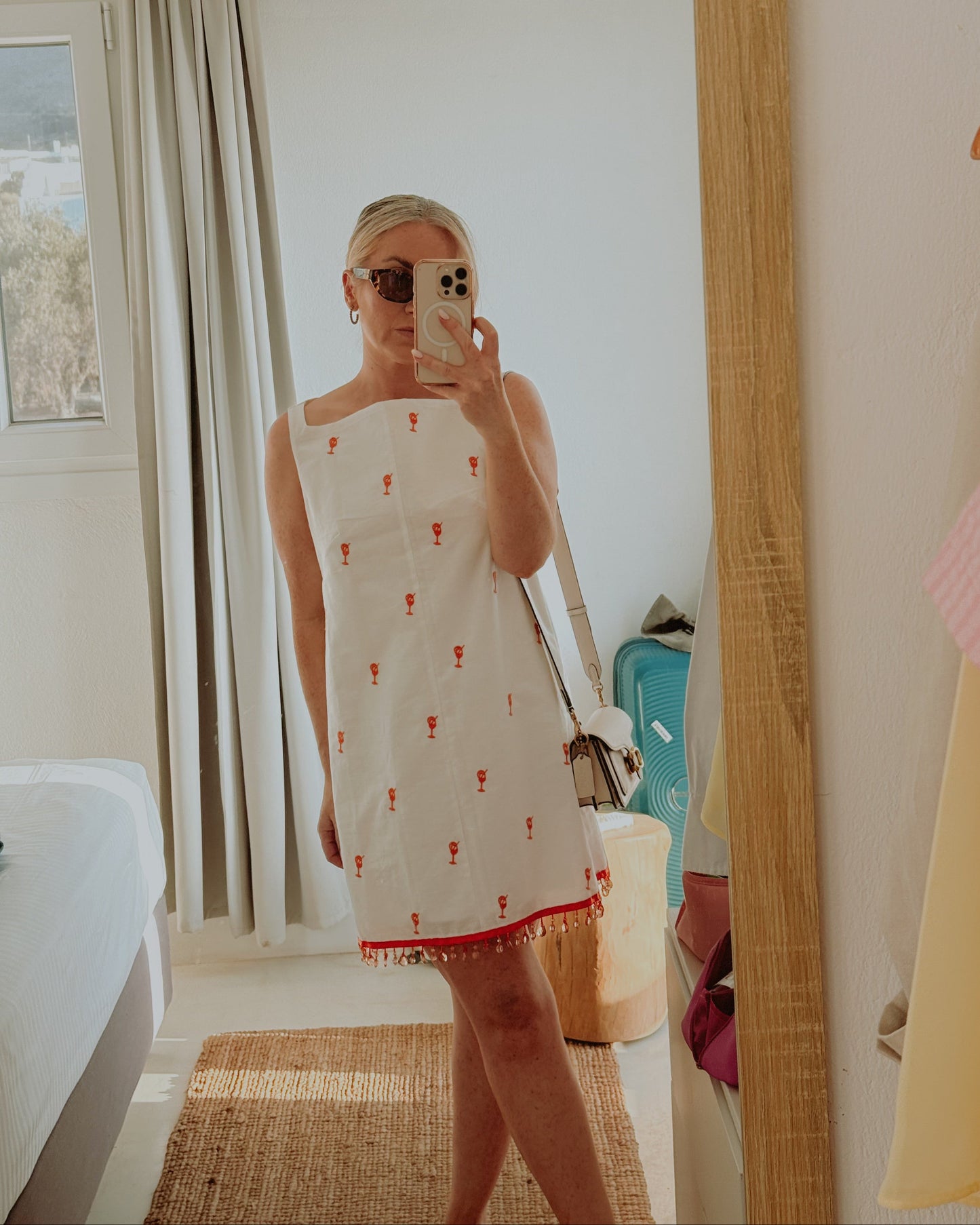 Person wearing a white dress with red patterns in a room.
