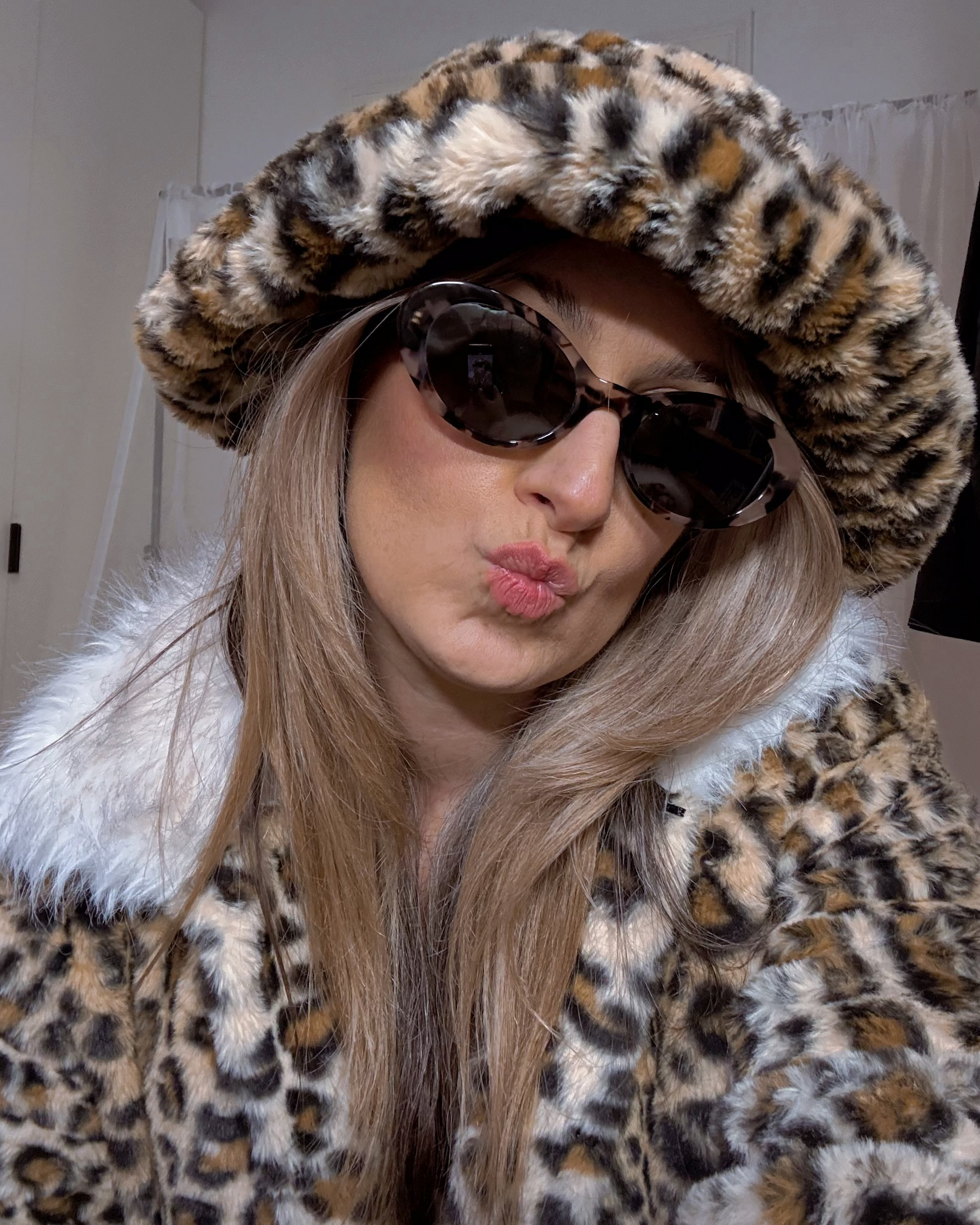 Person wearing a leopard print coat and hat with sunglasses, making a playful face.