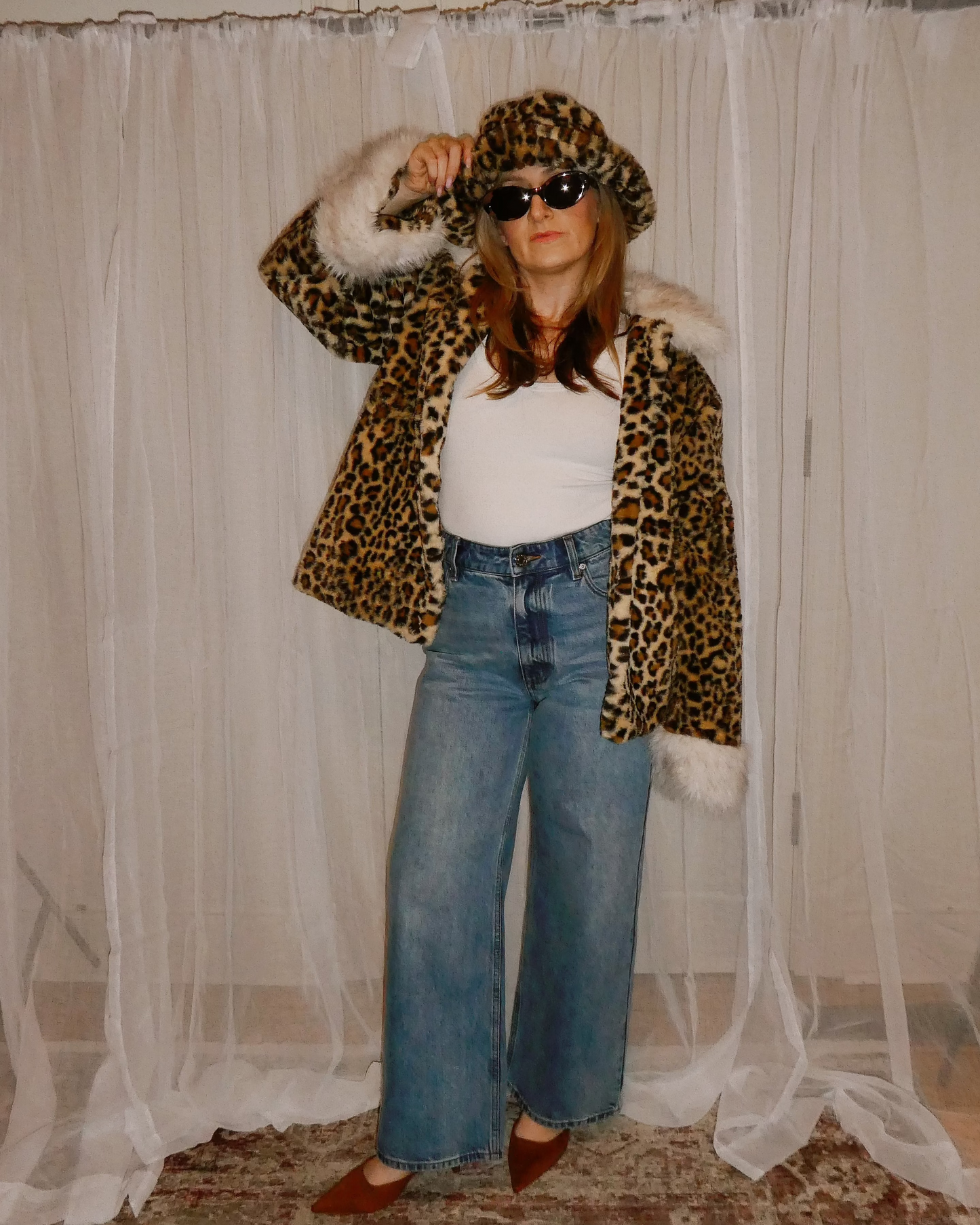 Person wearing a leopard print coat and sunglasses in front of a white curtain.