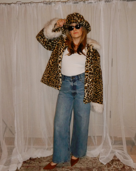 Person wearing a leopard print coat and sunglasses in front of a white curtain.