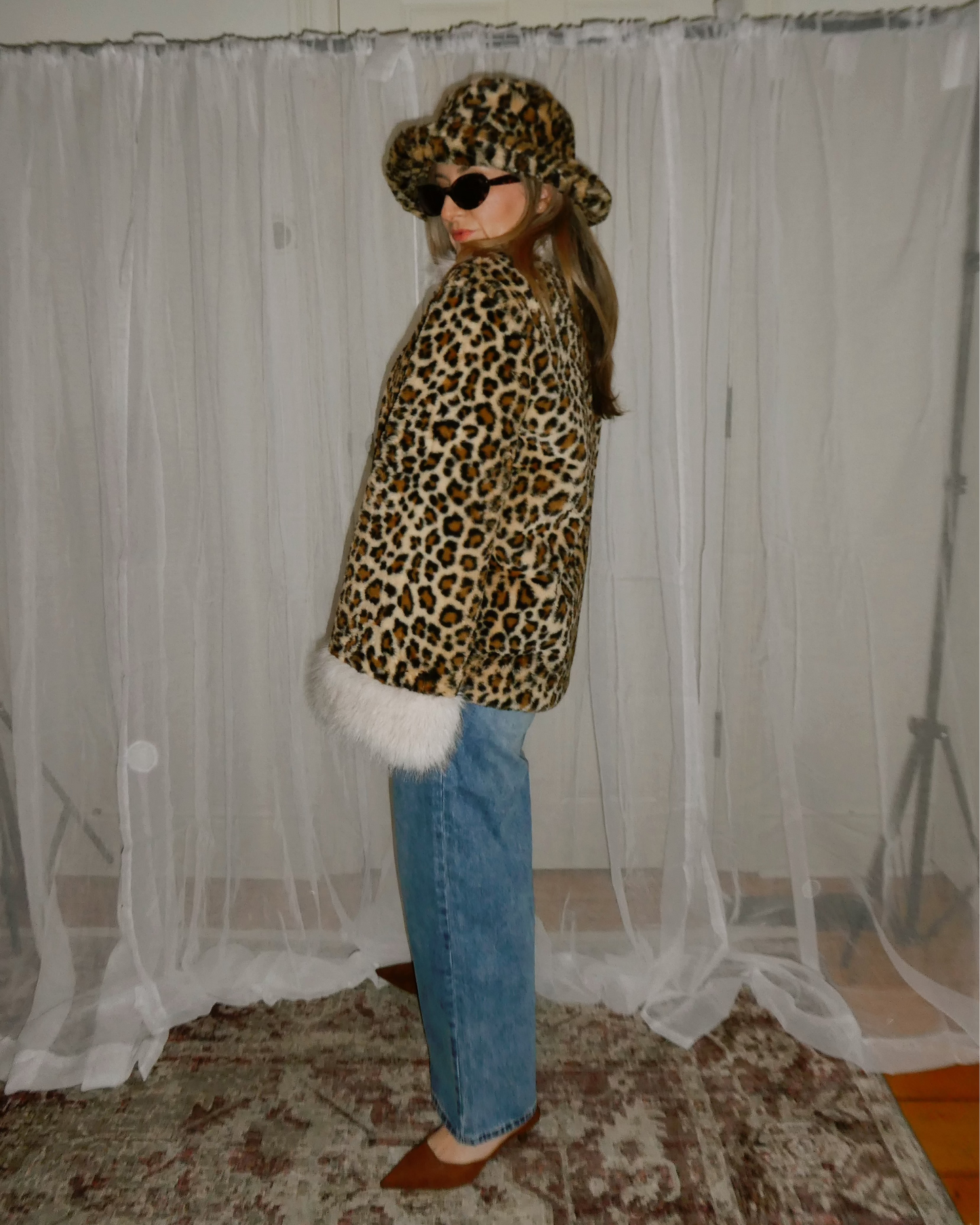 Person wearing a leopard print coat and hat in front of a white curtain