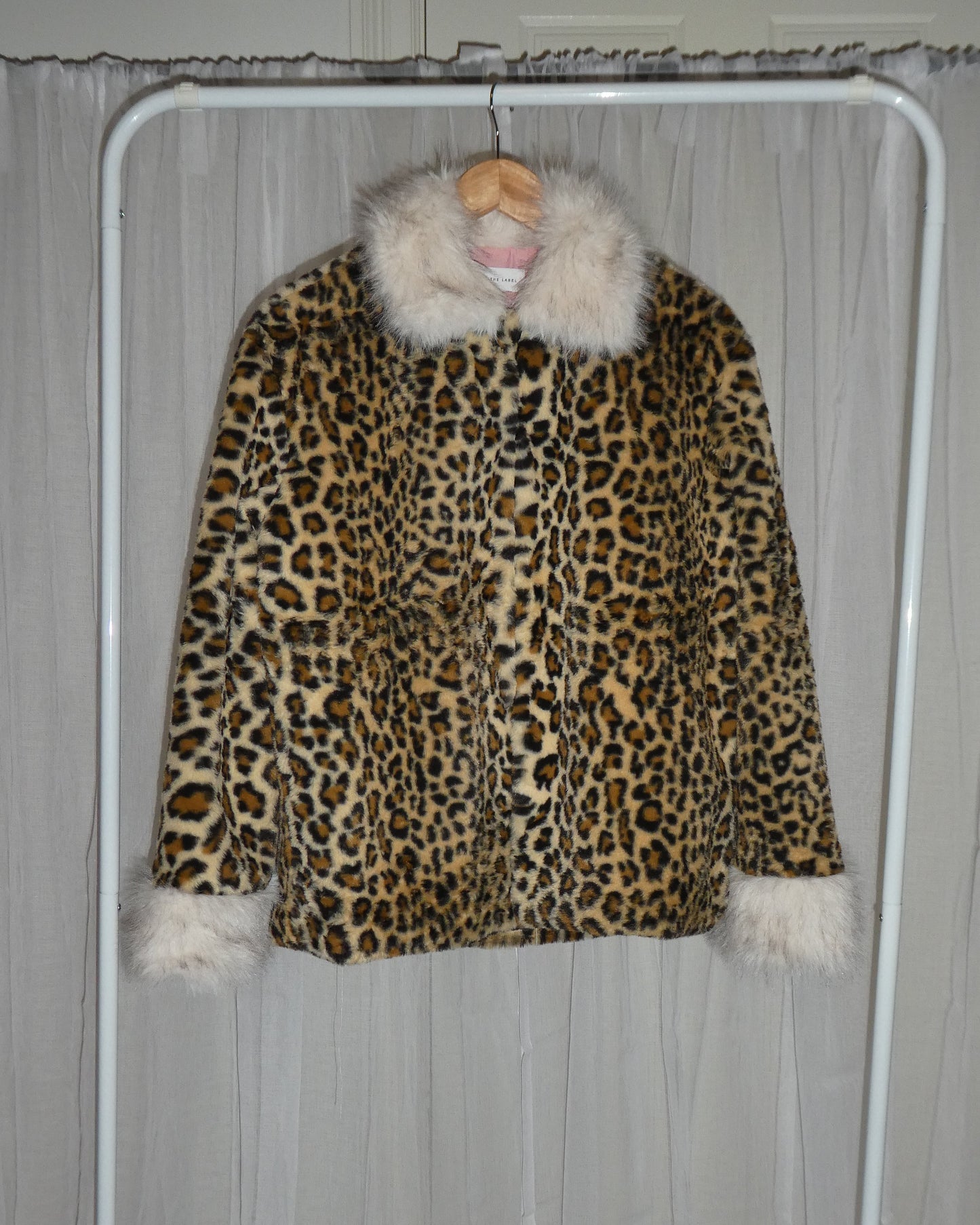 Leopard print coat with white fur trim hanging on a rack against a neutral background