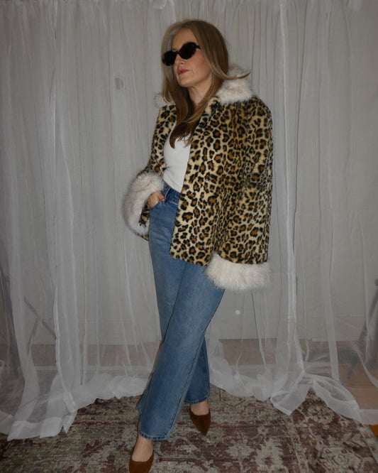 Woman wearing a leopard print coat with white fur trim, blue jeans, and sunglasses.
