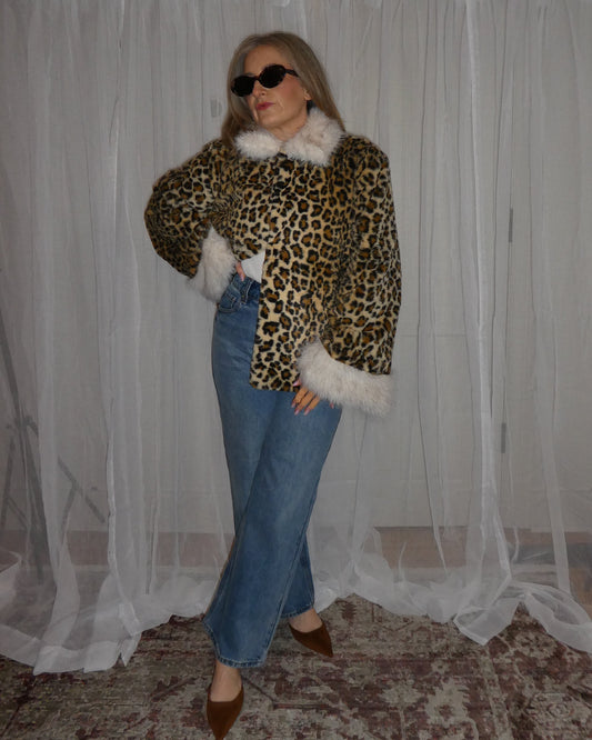 Person wearing a leopard print jacket with white fur trim in front of a white curtain.