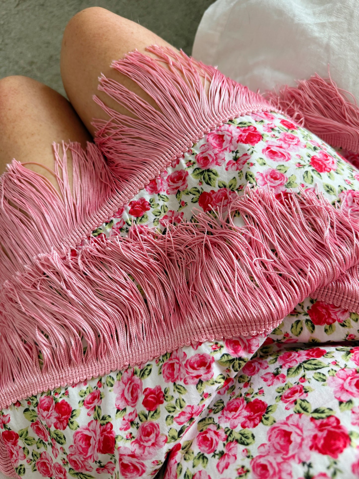 A close-up of a person wearing pink fringe shorts with a white background and a red and pink rose floral print.